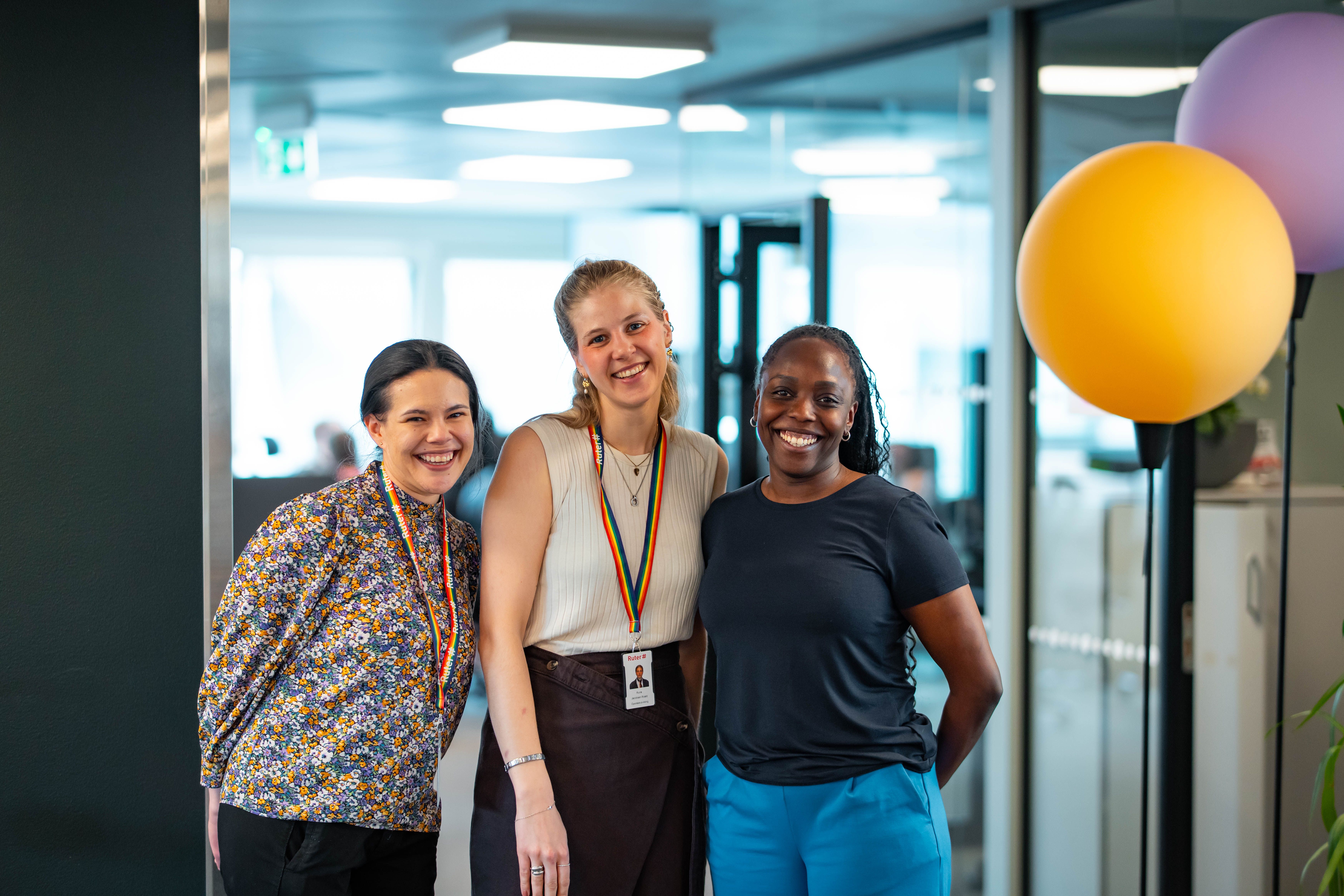 Tre kvinnelige, unge ansatte smiler i Ruters lokaler