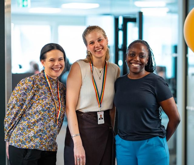 Tre kvinnelige, unge ansatte smiler i Ruters lokaler