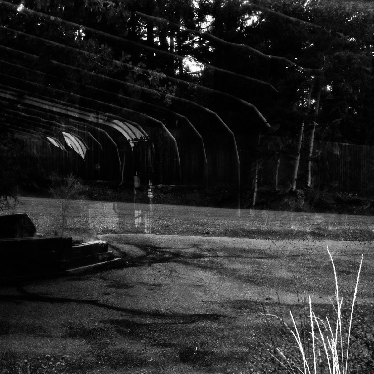 Ghostly arches drift over a dark scene, two moments laid on top of each other in grey.