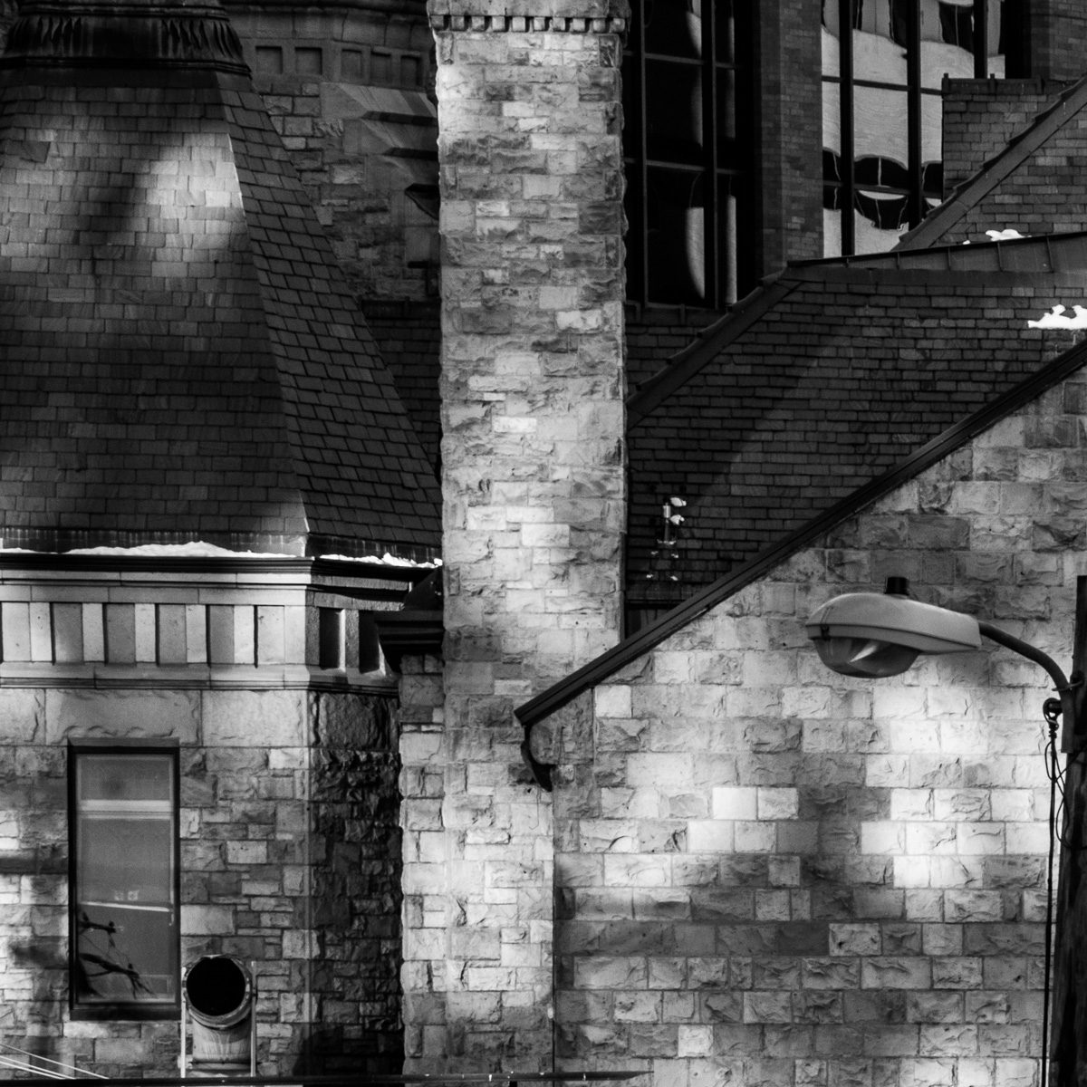 Black and white: stacked pale blocks and dark slanted planes interlock, dappled with blurred patches of light.