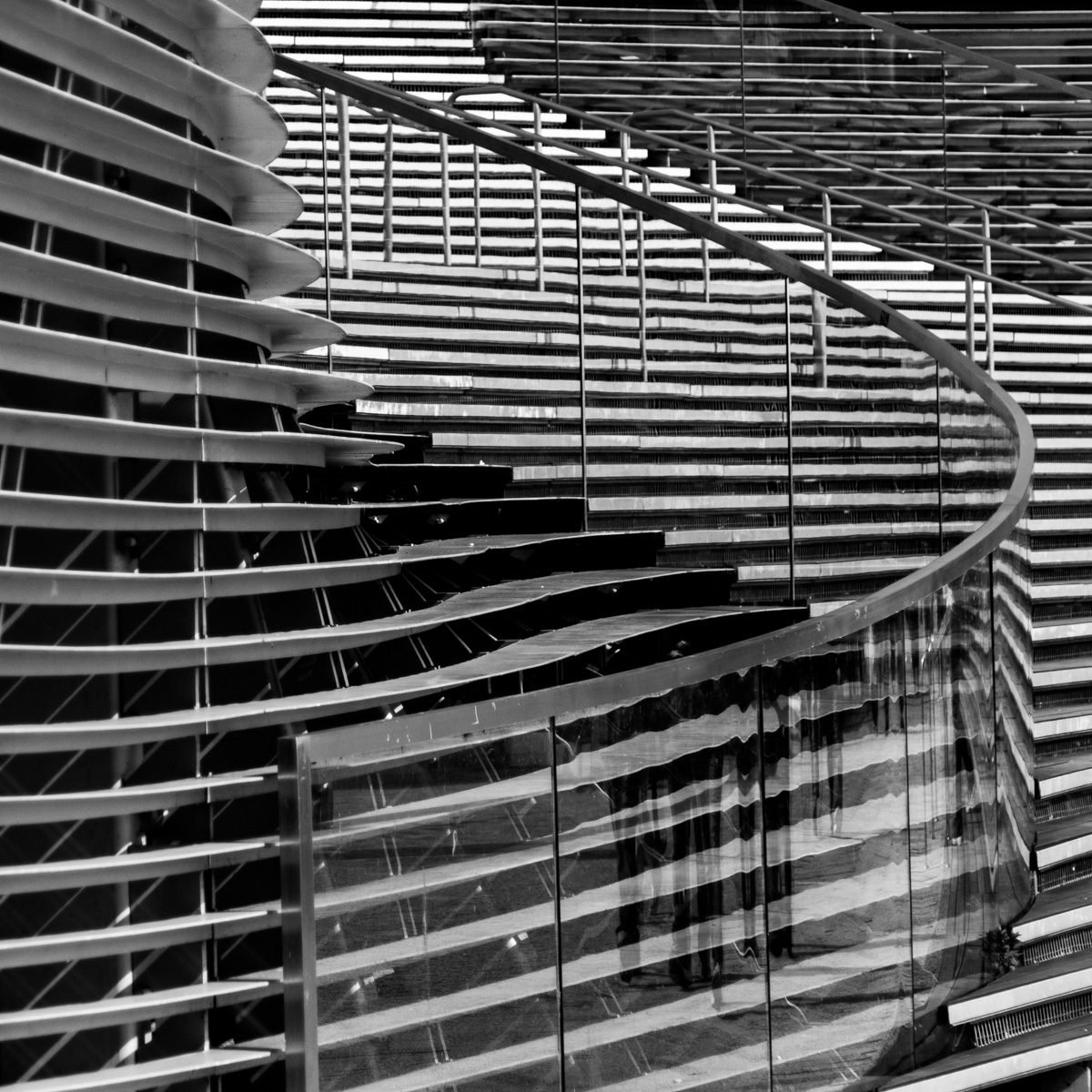 Black and white: tiers of thin horizontal slats curve around from the left, with a smooth dark line sweeping through them in a long S.