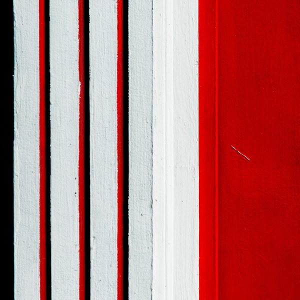 Vertical stripes of white and deep red with thin black gaps, widening into a solid red field on the right.