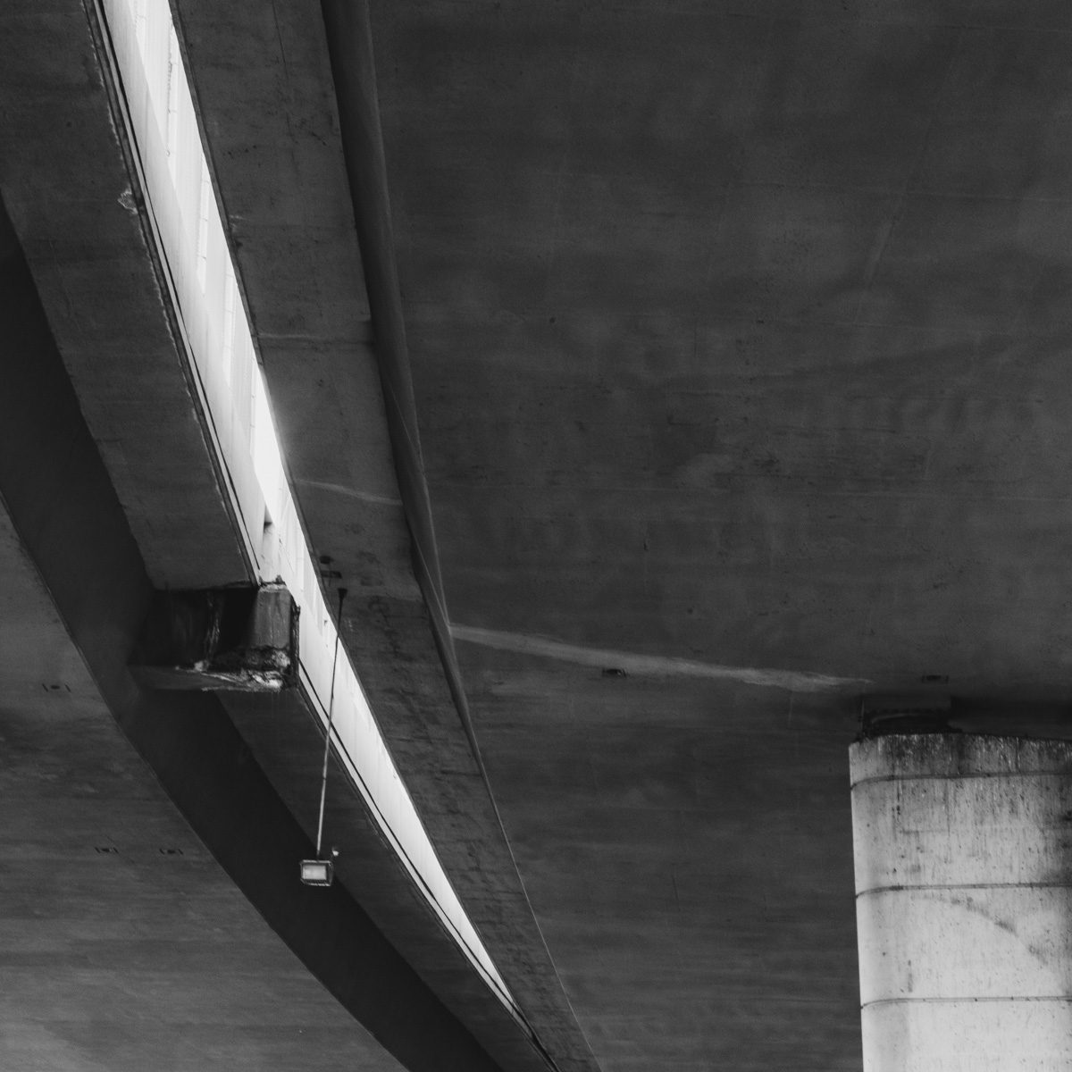 Black and white: a long pale curve sweeps down from the top left across a dark grey expanse, meeting a squat pale upright block in the lower right.