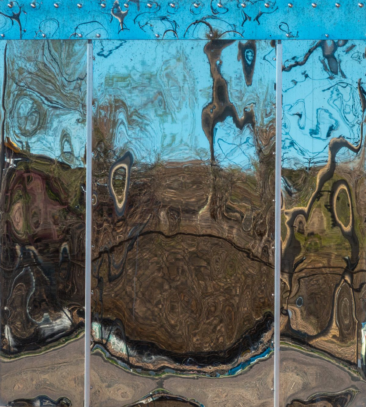 Three tall panels of warped, swirling colour, pale blue above and brown below, separated by thin silver uprights and topped by a blue band studded with small dots.