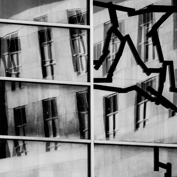 Black and white: a grid of tilted pale rectangles and dark slots, split by bold lines and crossed by a jagged black zigzag on the right.