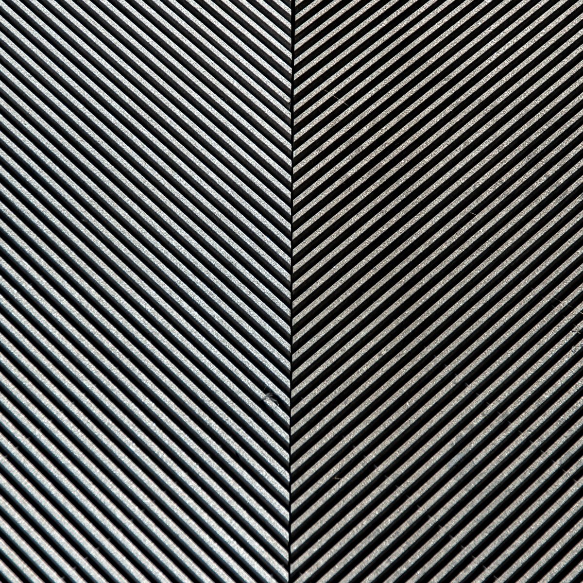 Fine diagonal ridges of silver and black, running one way on the left and the opposite way on the right, meeting at a thin vertical seam.