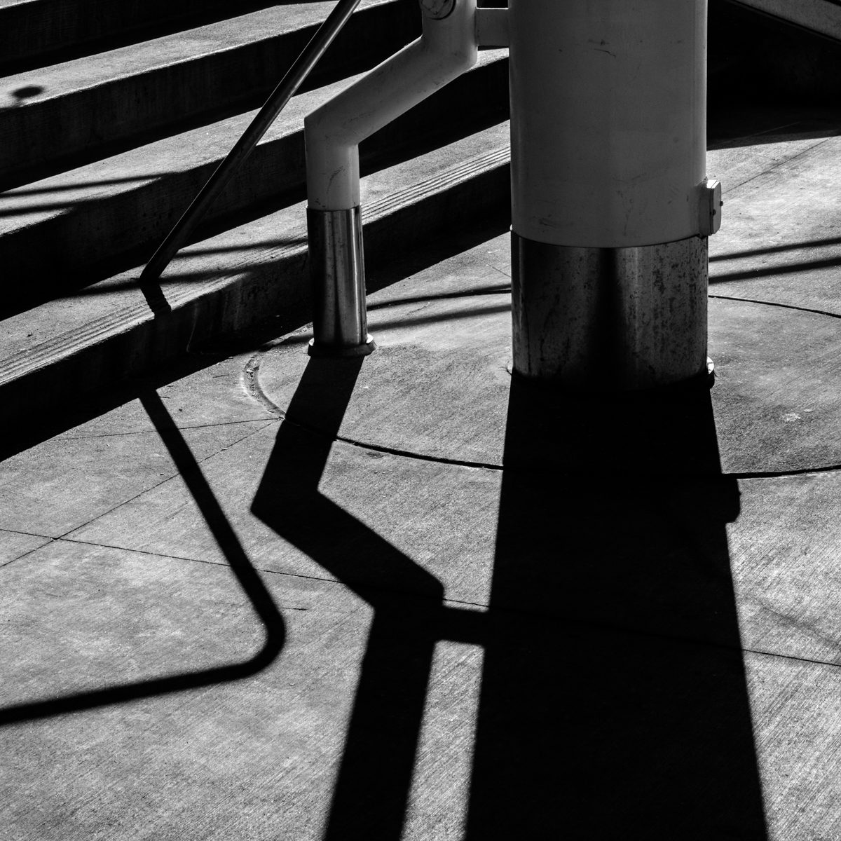 Hard black shadows bend and zigzag across pale ground beside a white upright.