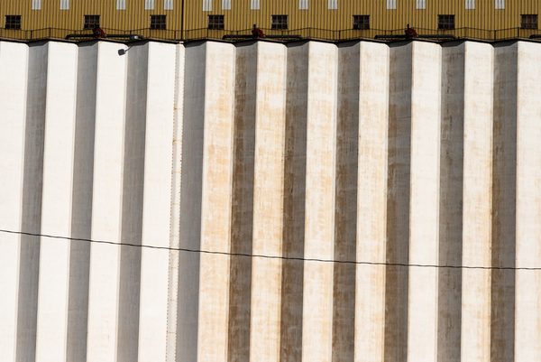 A wide picture of tall vertical bands in cream and pale grey, some stained orange, beneath a strip of olive with small dark squares, crossed by one thin sagging line.