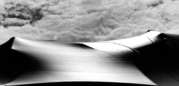 A wide black and white picture: a dark curving form with a glinting ridge stretches across the middle beneath a band of billowing pale grey.