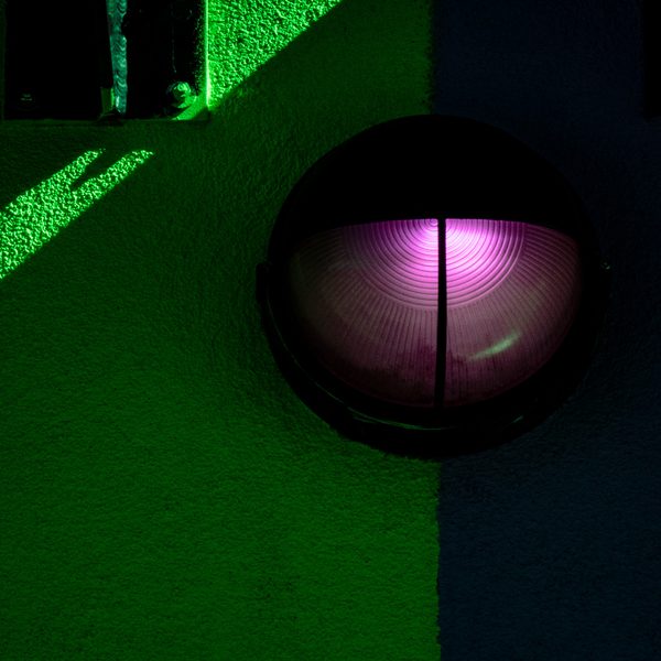 A glowing pink half-circle inside a black dome, set against acid green and deep navy divided by a hard vertical edge.
