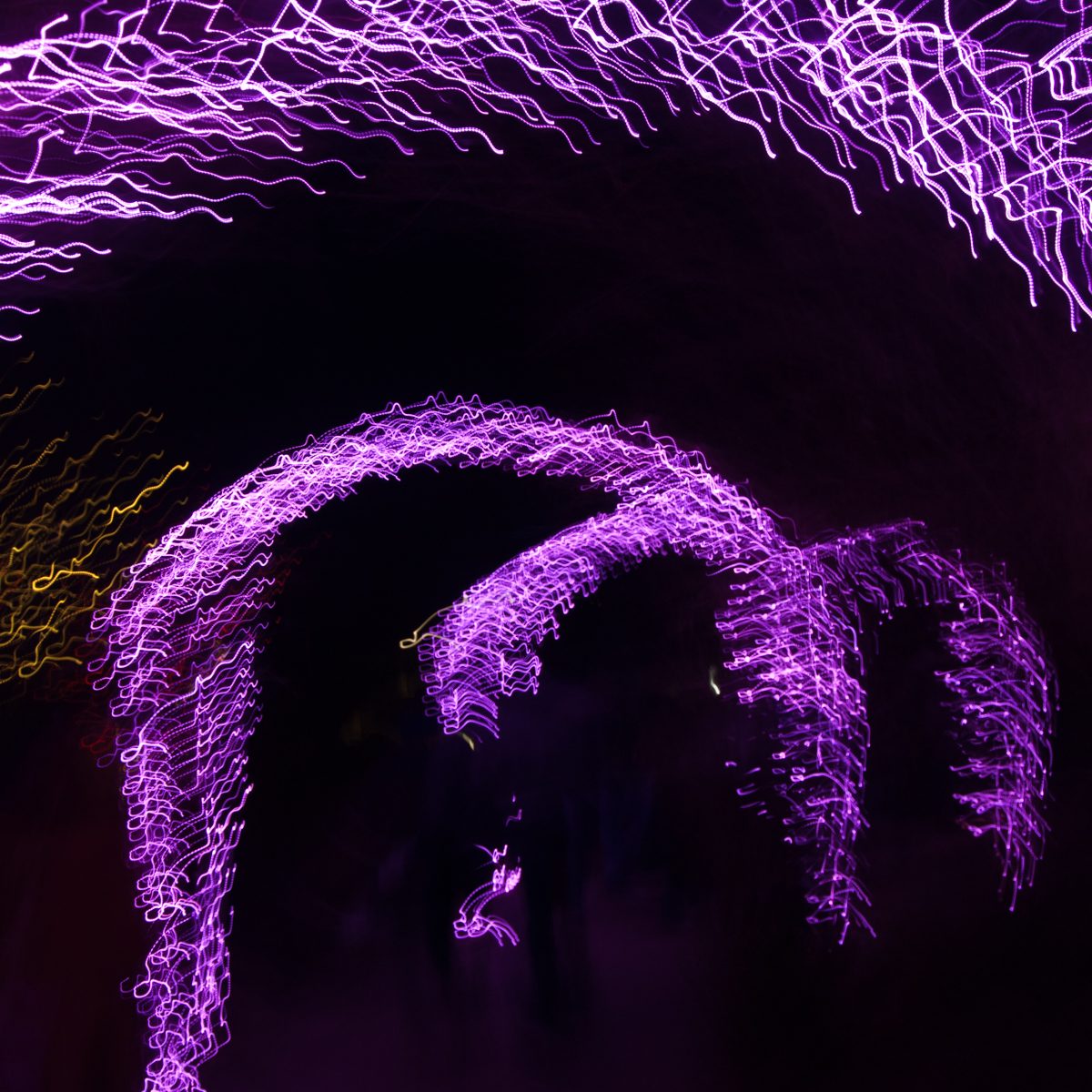 Fizzing violet lines loop into two arches across near-black, with a faint thread of gold at the left edge.
