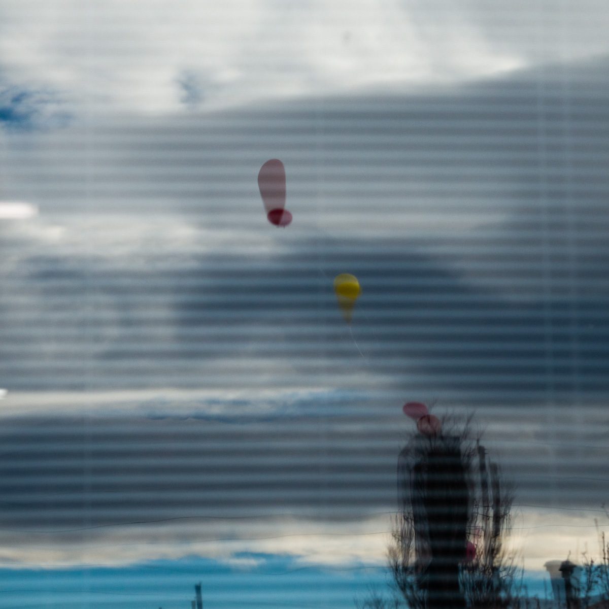 Fine horizontal lines stripe a field of slate grey, blue and white, with a few small red and yellow ovals floating in it and a dark blurred shape rising at the bottom.