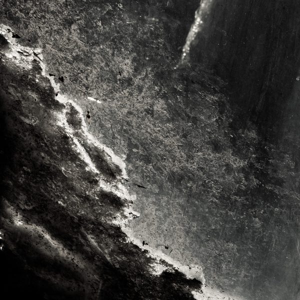 Black and white: a coarse speckled surface split by a bright jagged edge running diagonally, with deep shadow at the left.