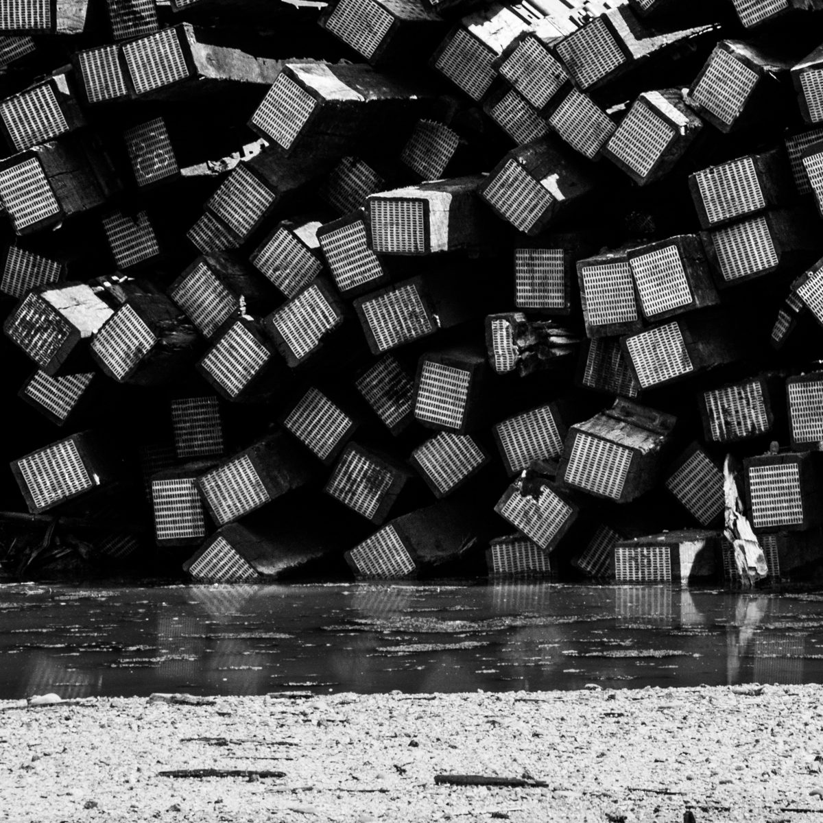 Dozens of striped blocks tumble over one another in a dark heap, above a thin bright strip and pale speckled ground.