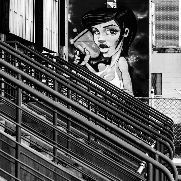 Black and white: a dense run of dark parallel bars steps down diagonally in front of a large pale shape and pale grid-patterned blocks.