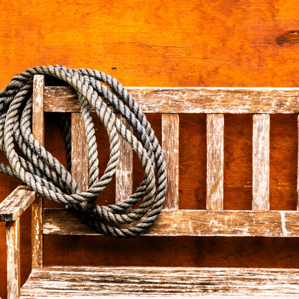 Thick grey coils loop over a weathered bench against glowing orange.