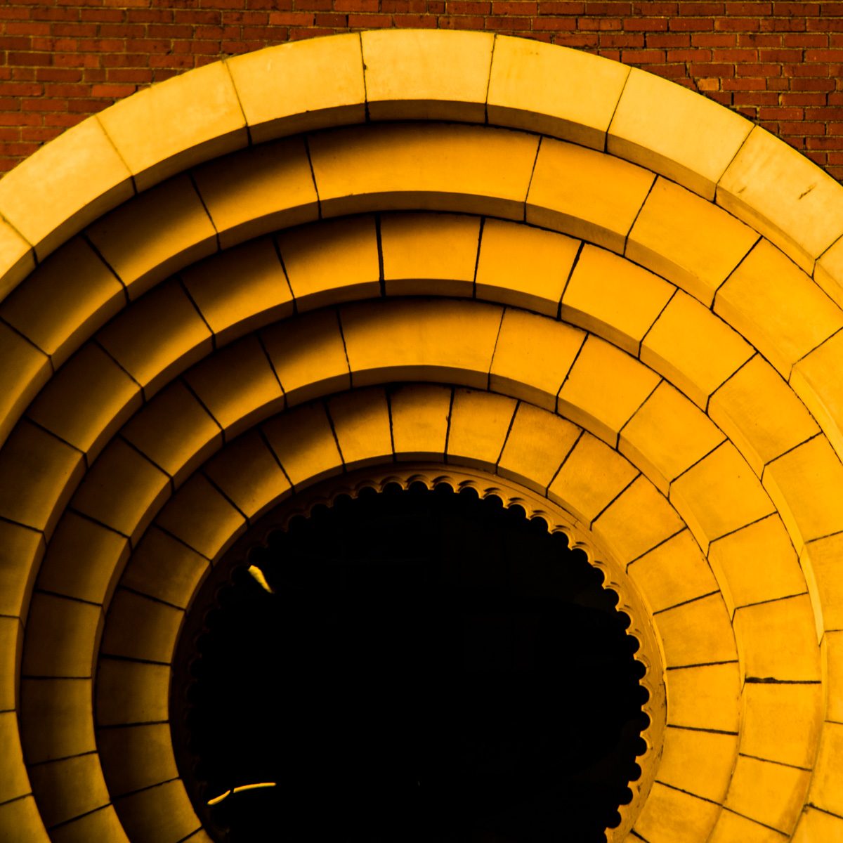 Concentric arcs of glowing yellow segments narrowing toward a black circle with a toothed edge, under a strip of rust red.