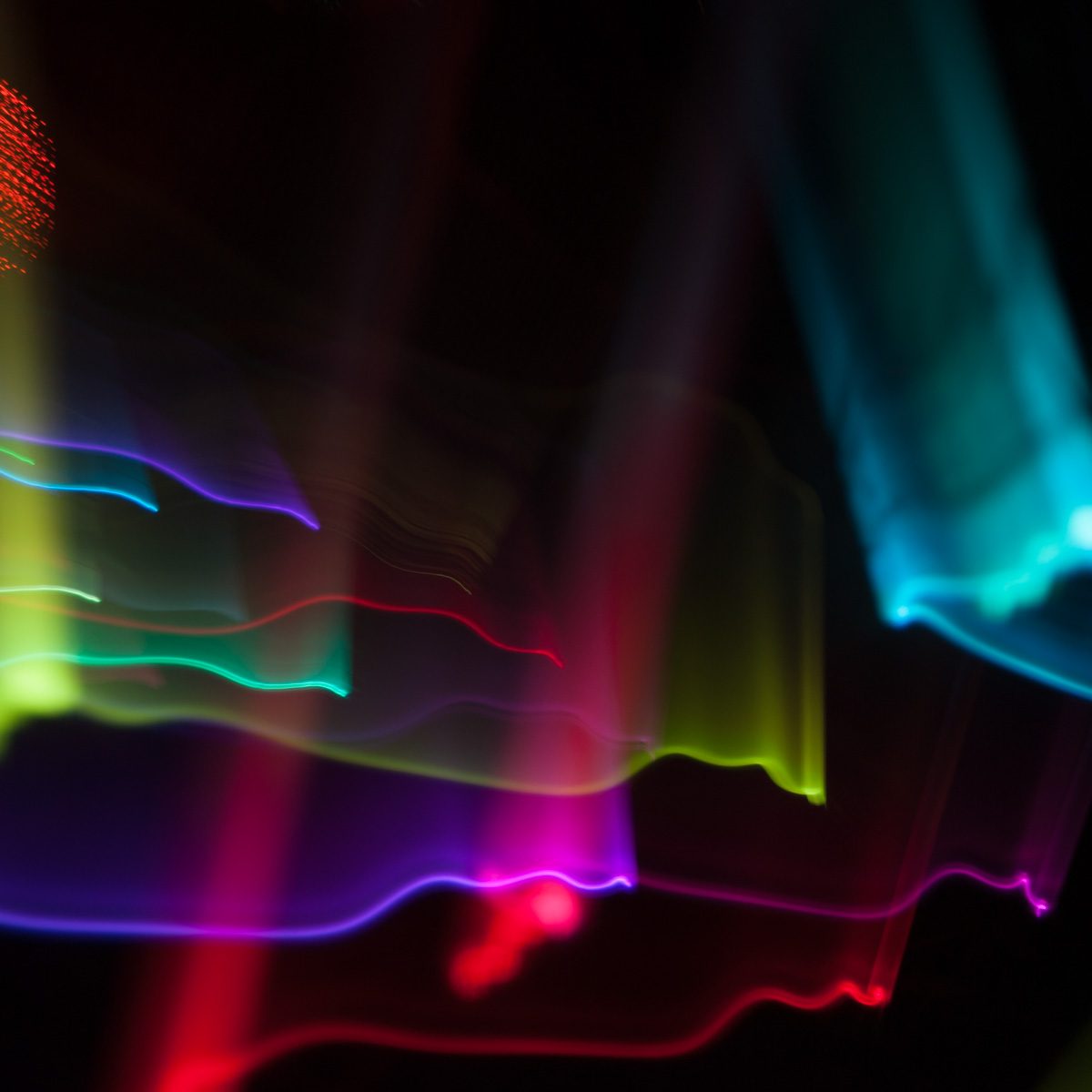 Ribbons of violet, green, cyan and red trail horizontally across black, blurred and overlapping.