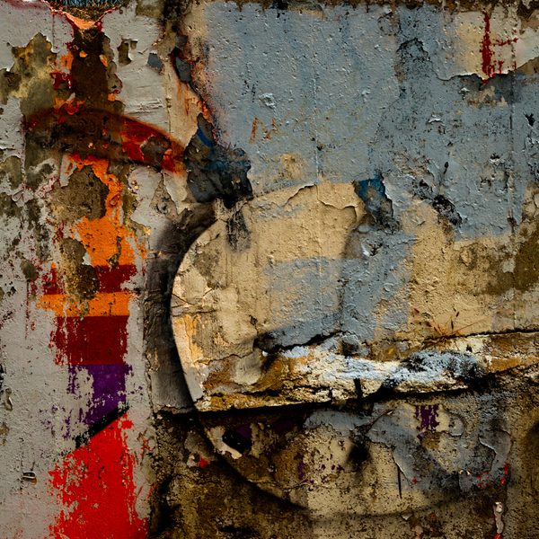 Peeling layers of blue grey, ochre and cream around a pale half-disc, with bright streaks of orange, red and purple down the left.