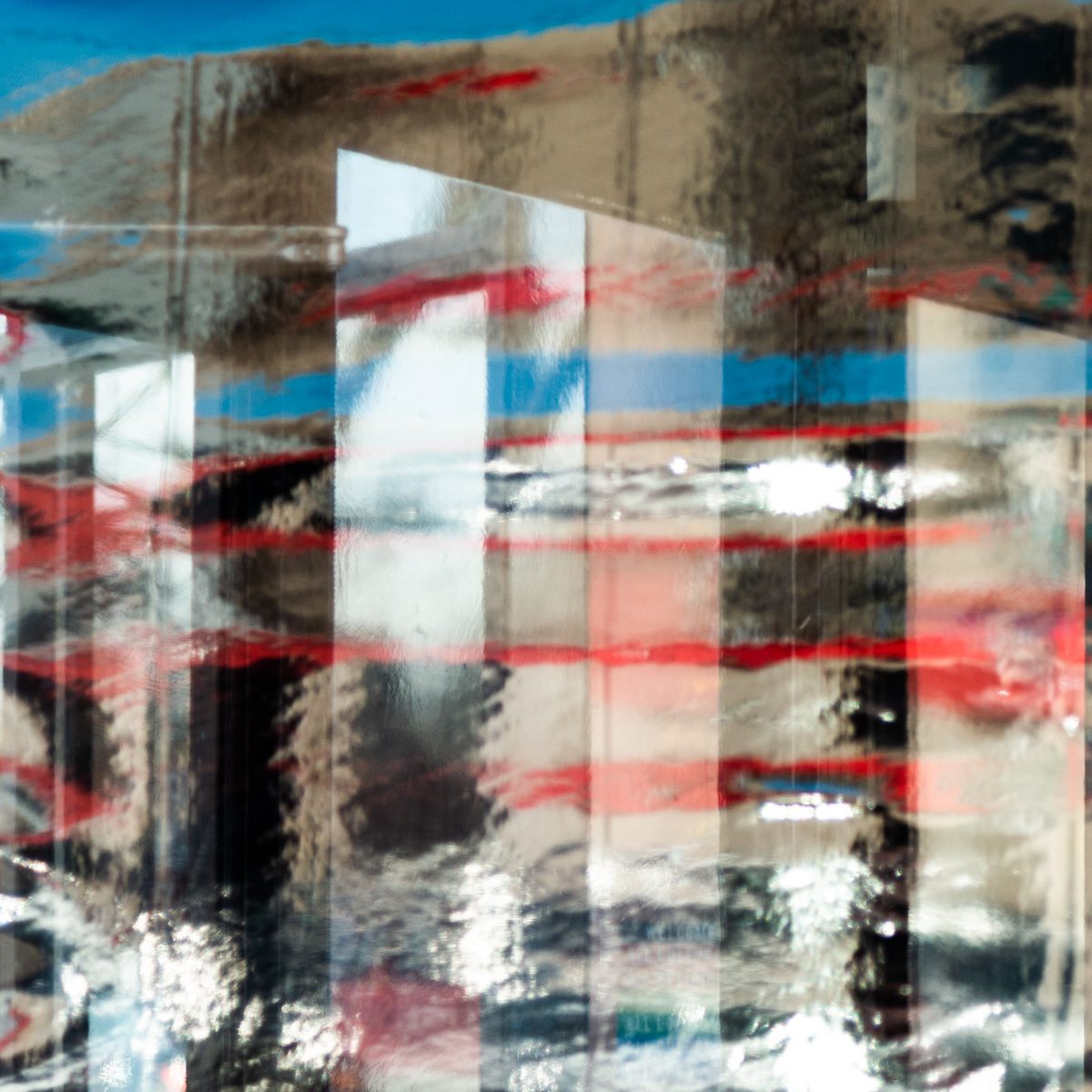 Red and blue streaks bend across pale upright panels that ripple and shimmer like heat.