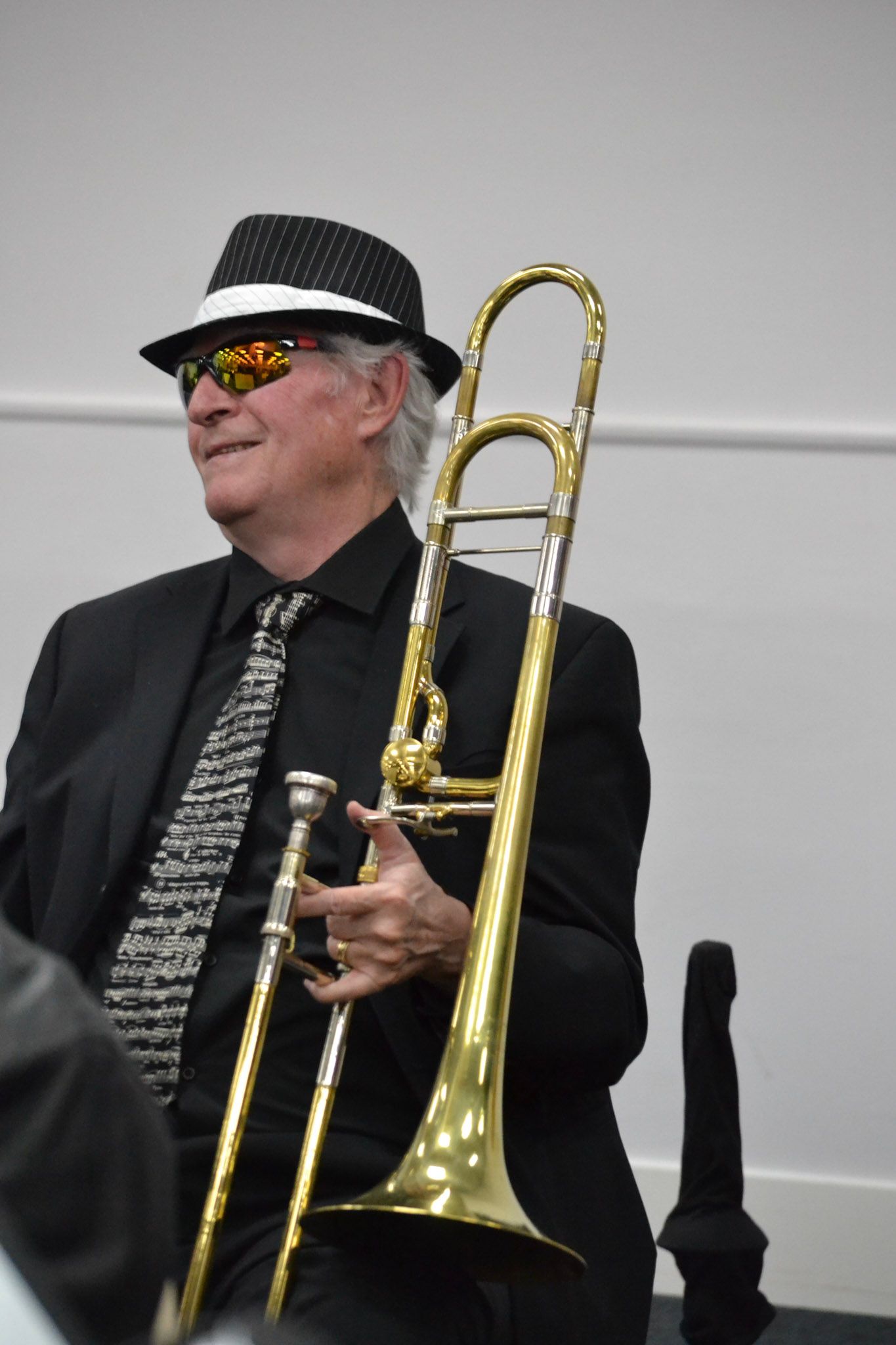 A SwingMasters trombonist in sunglasses and a fedora holding his trombone
