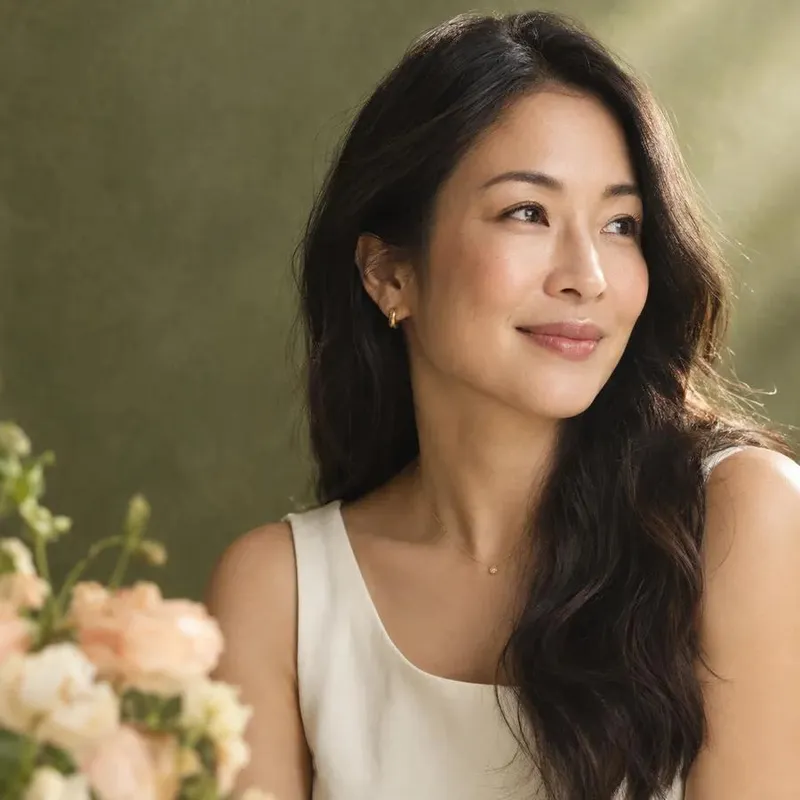 Smiling woman in a cream top beside a bunch of flowers