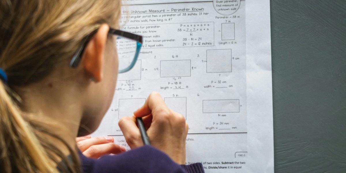 A teenage girl with glasses working on a math worksheet, seen from behind