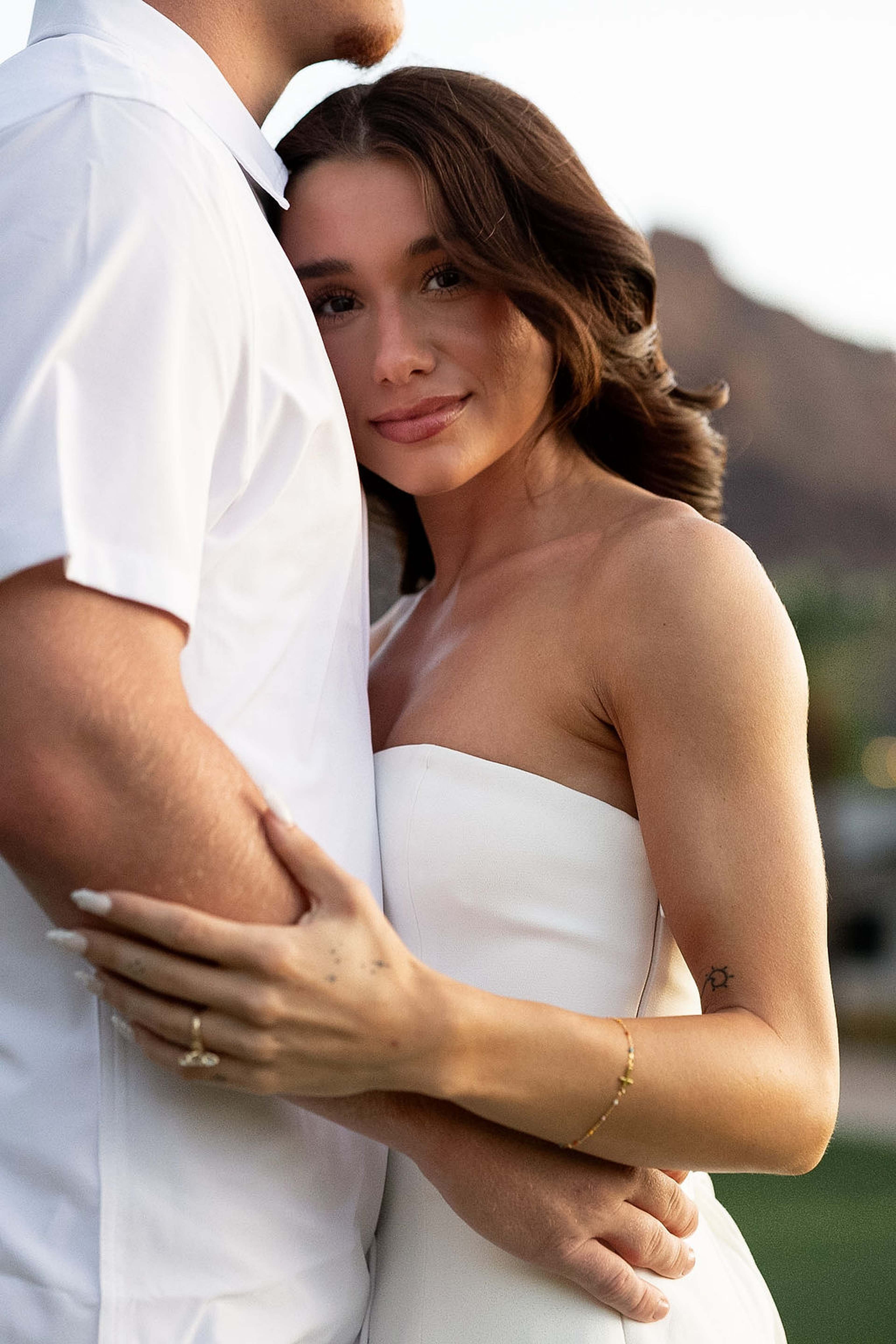 Detail of a couple's arms wrapped around each other, her hand resting over his, thin gold bracelet catching the light