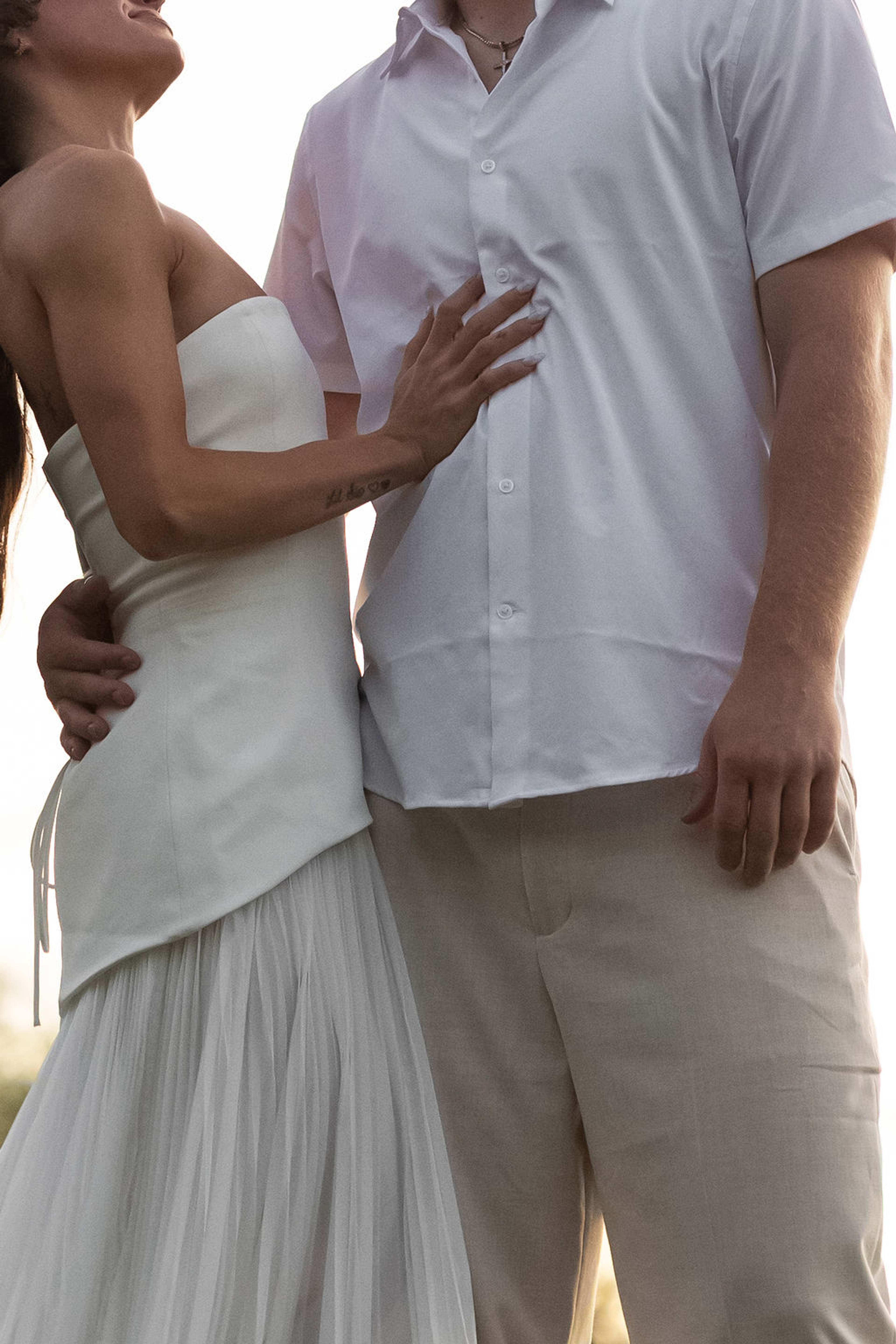Close detail of a couple's hands at her waist, pleated white fabric and a linen shirt