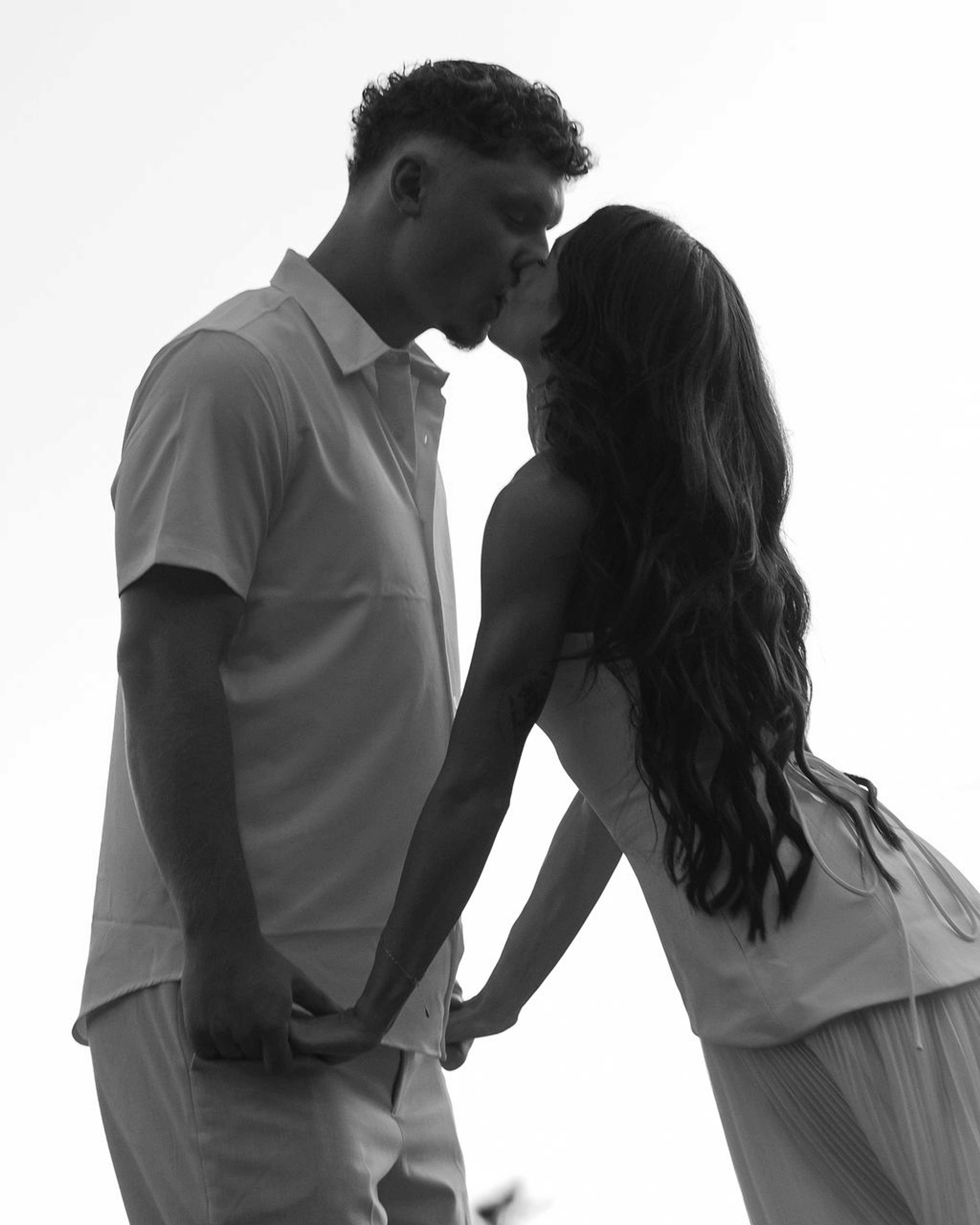 Black and white frame of a couple leaning in to kiss, hands clasped low between them