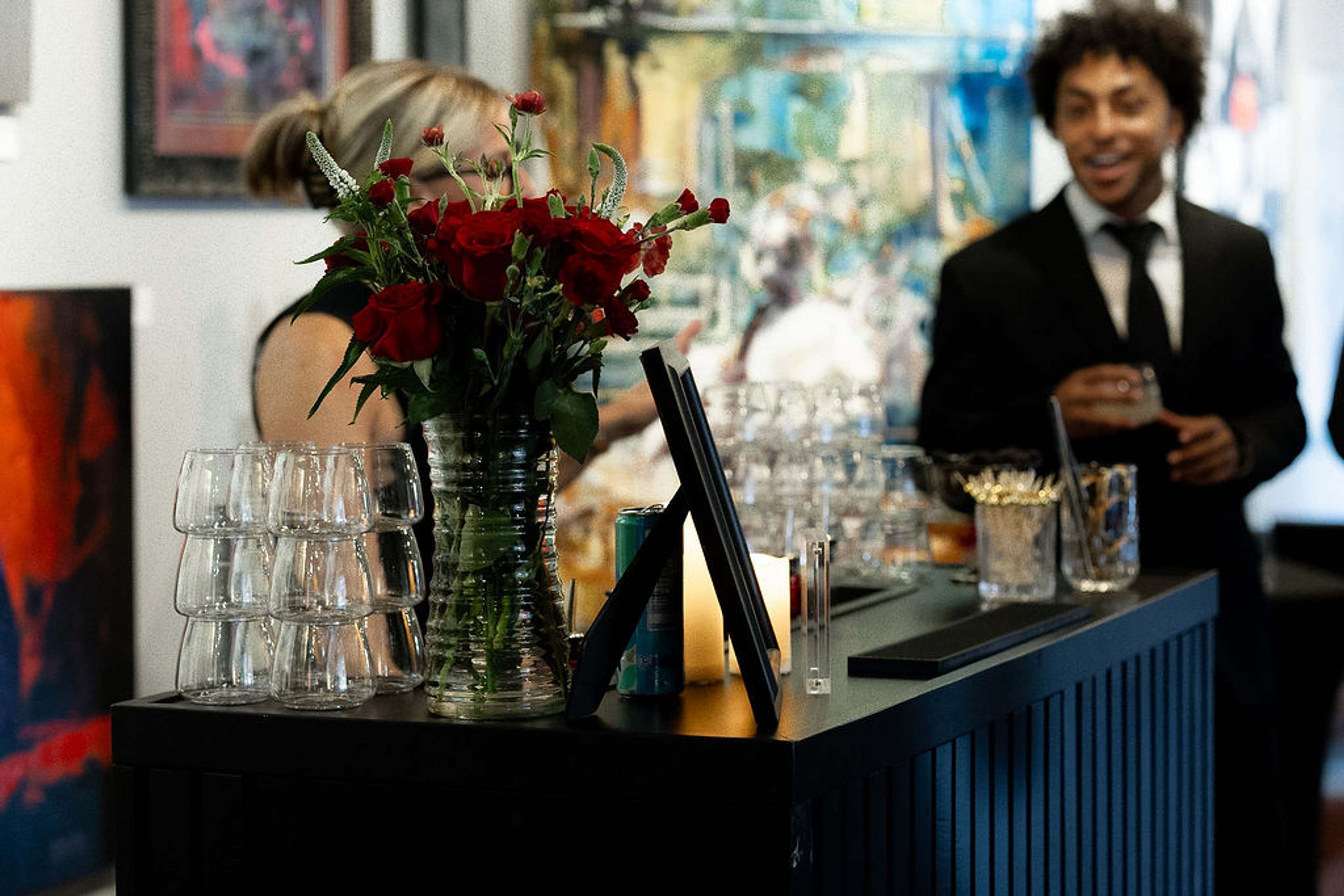 Red roses and stacked glassware on the bar, a guest smiling behind