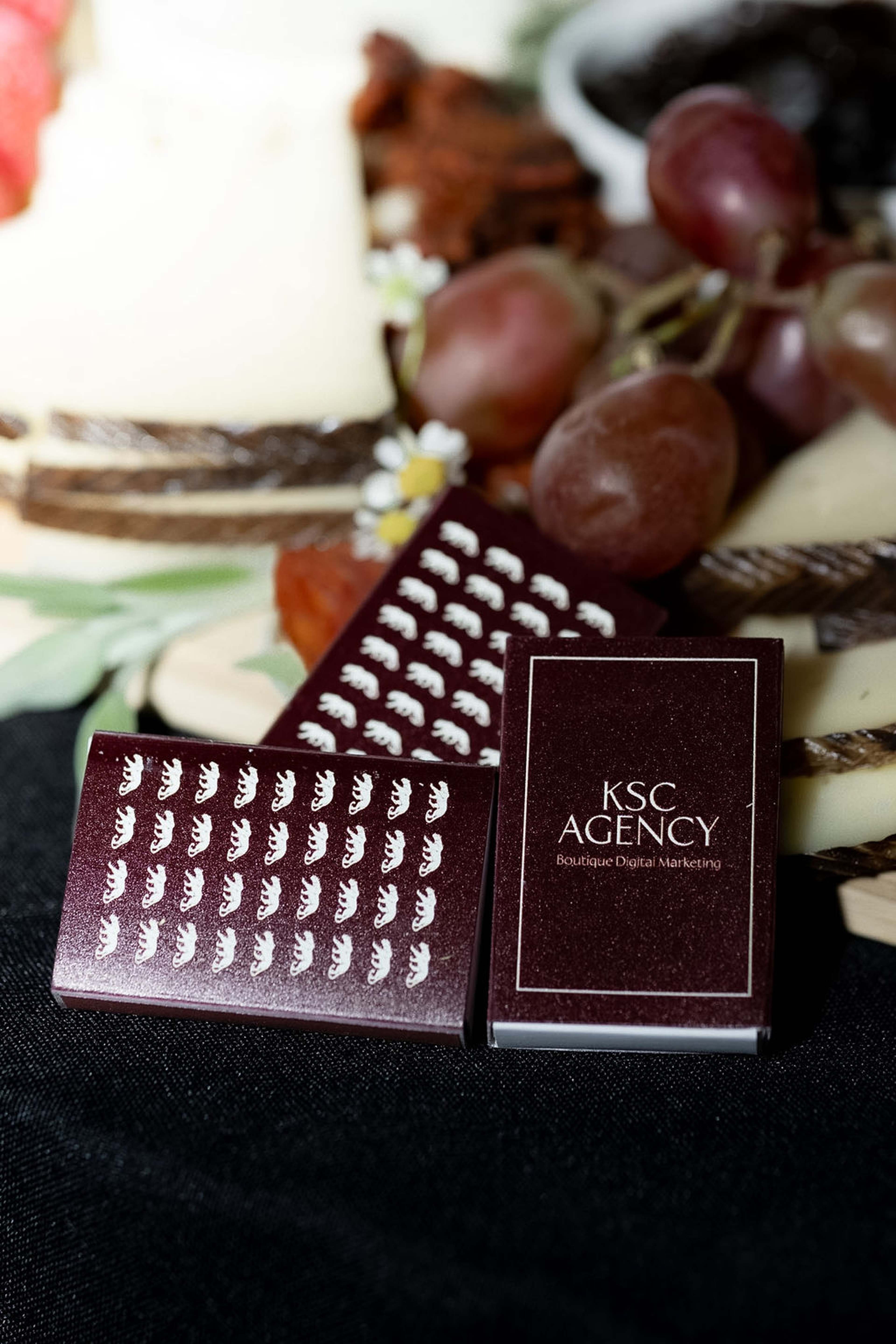 A KSC Agency chocolate bar and branded card styled on a grazing board with grapes and cheese