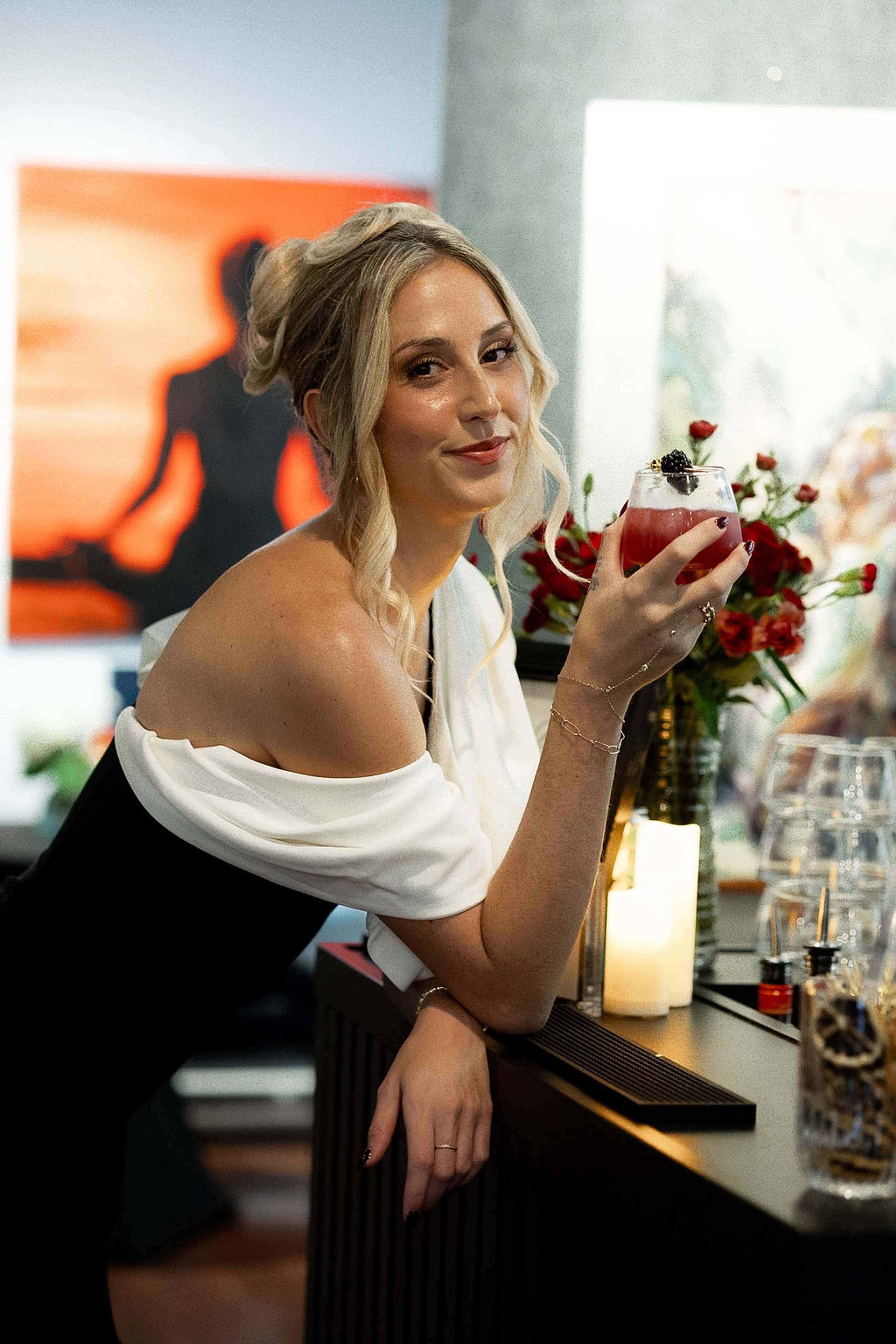 Guest at the bar with a berry cocktail, red roses and artwork behind
