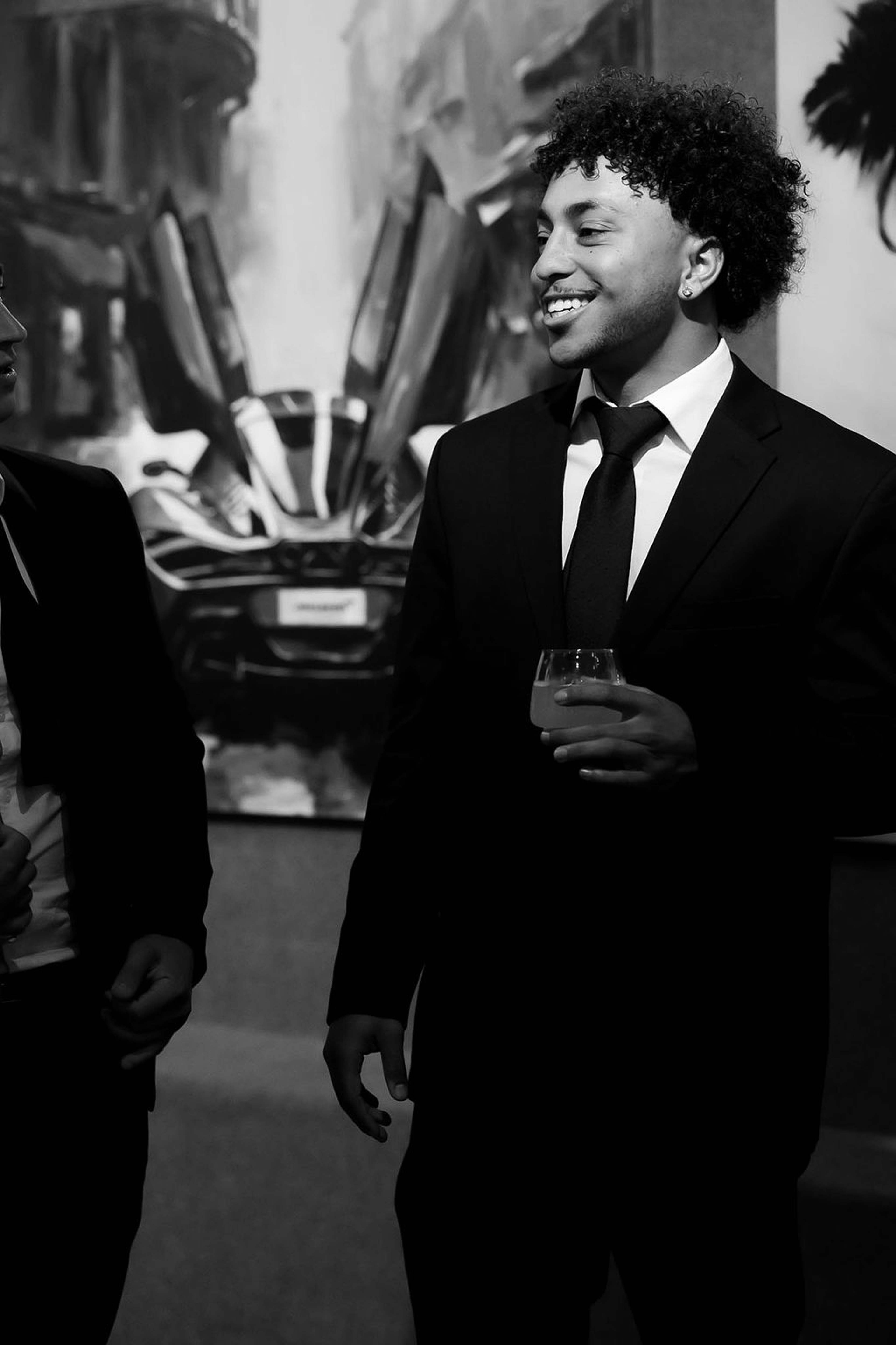 Two guests in black tie in conversation beside a large painting of a car