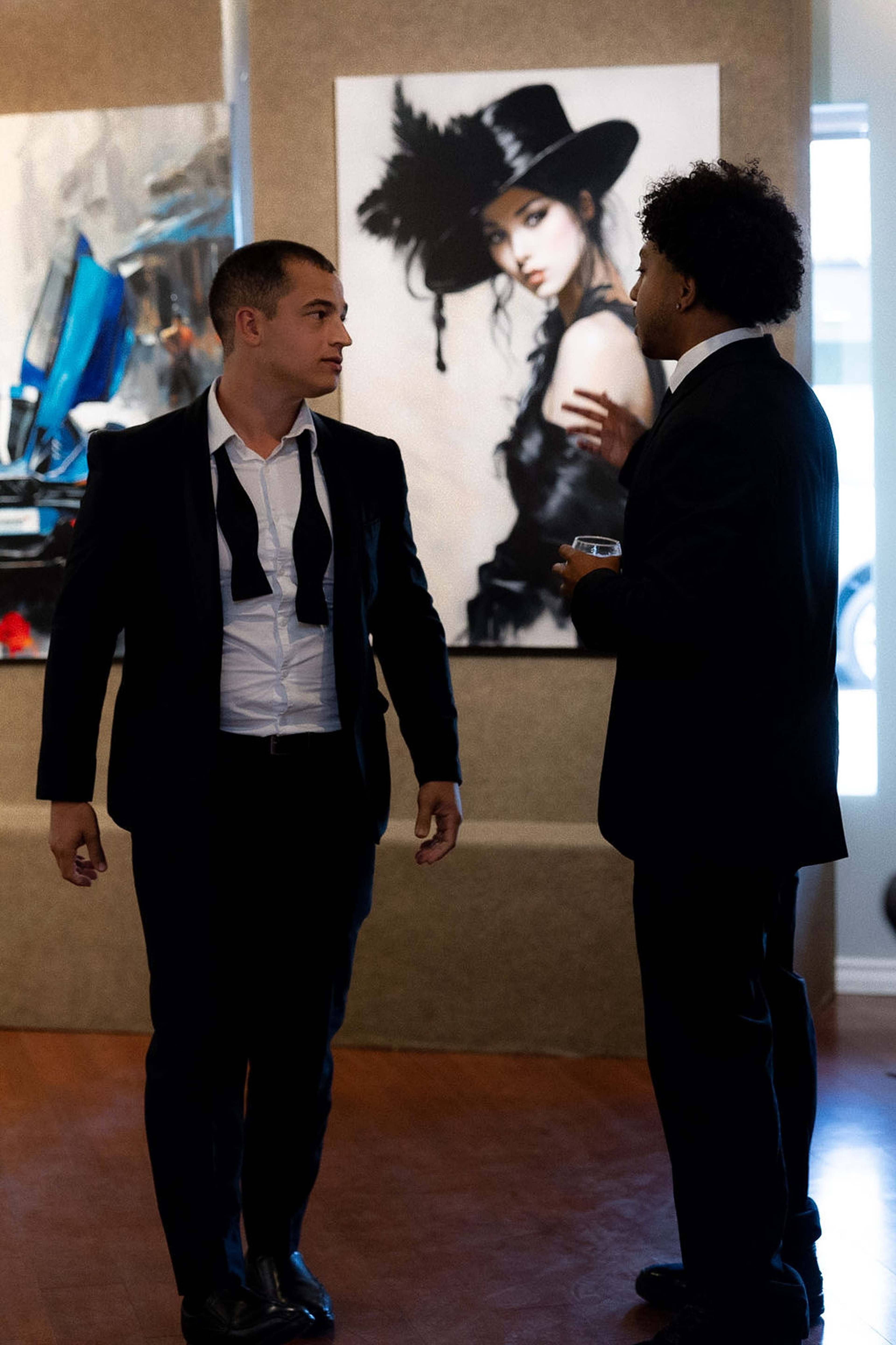 Two guests in dark suits talking in front of a portrait painting