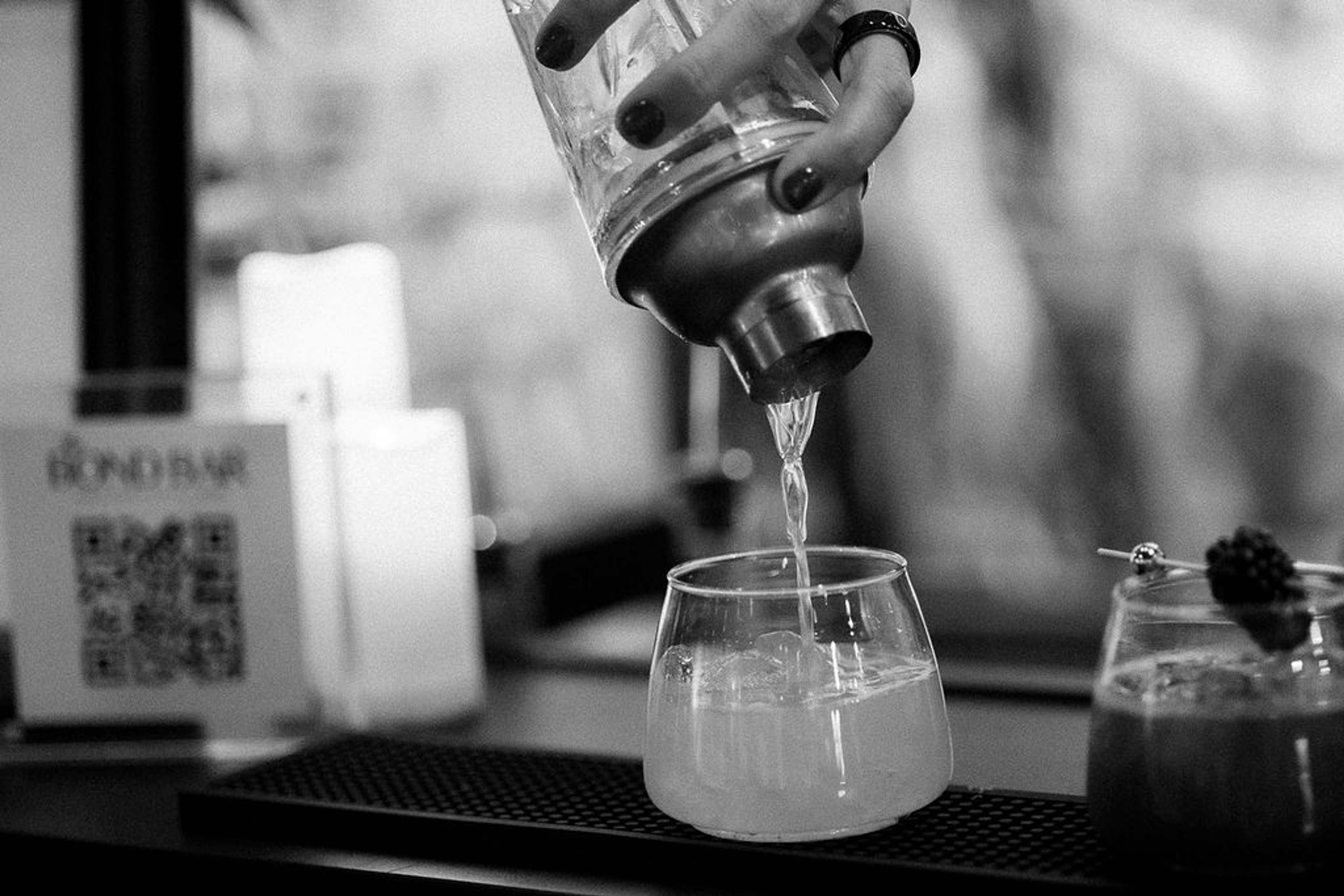 Black and white detail of a cocktail strainer pouring into a stemless glass