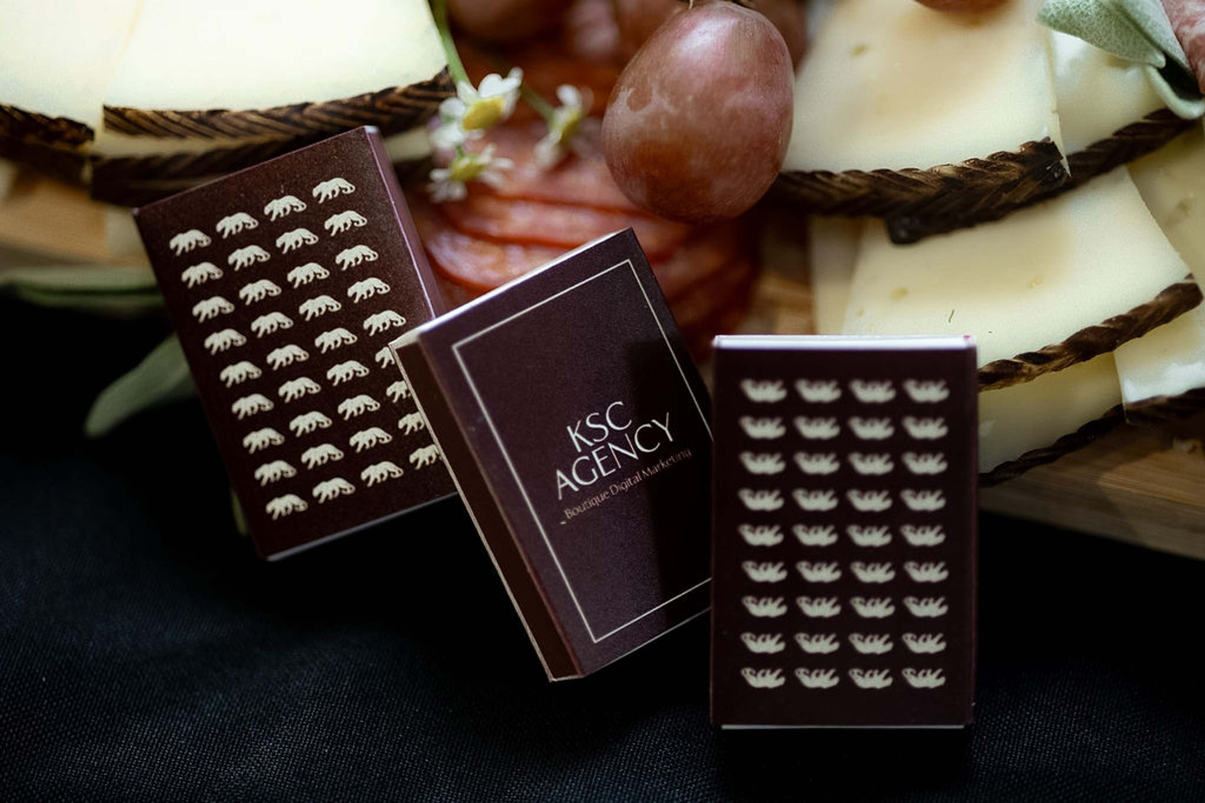 A KSC Agency branded chocolate bar standing on a charcuterie board among grapes and cured meats