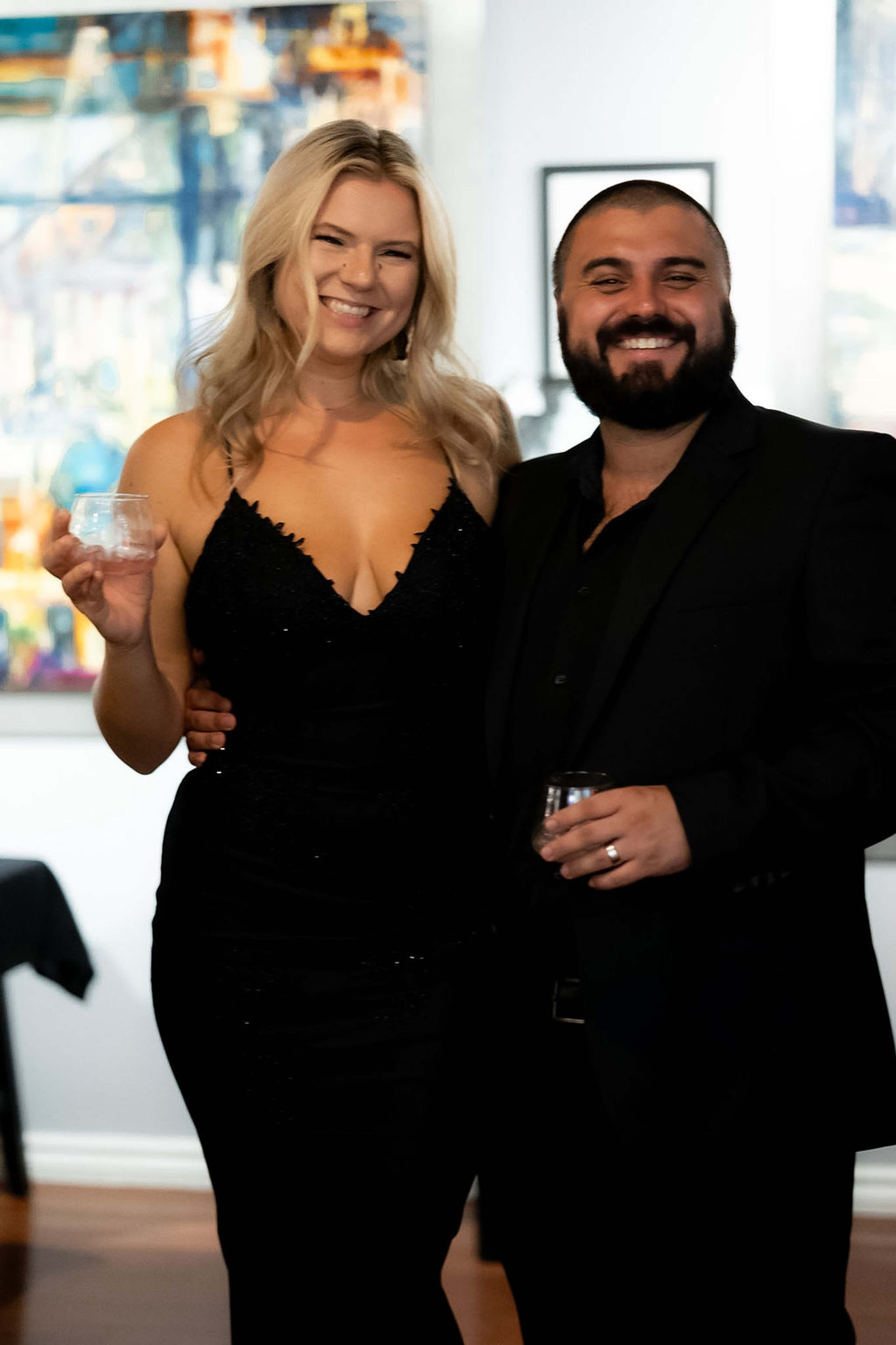 A couple posed together, drinks in hand, artwork behind
