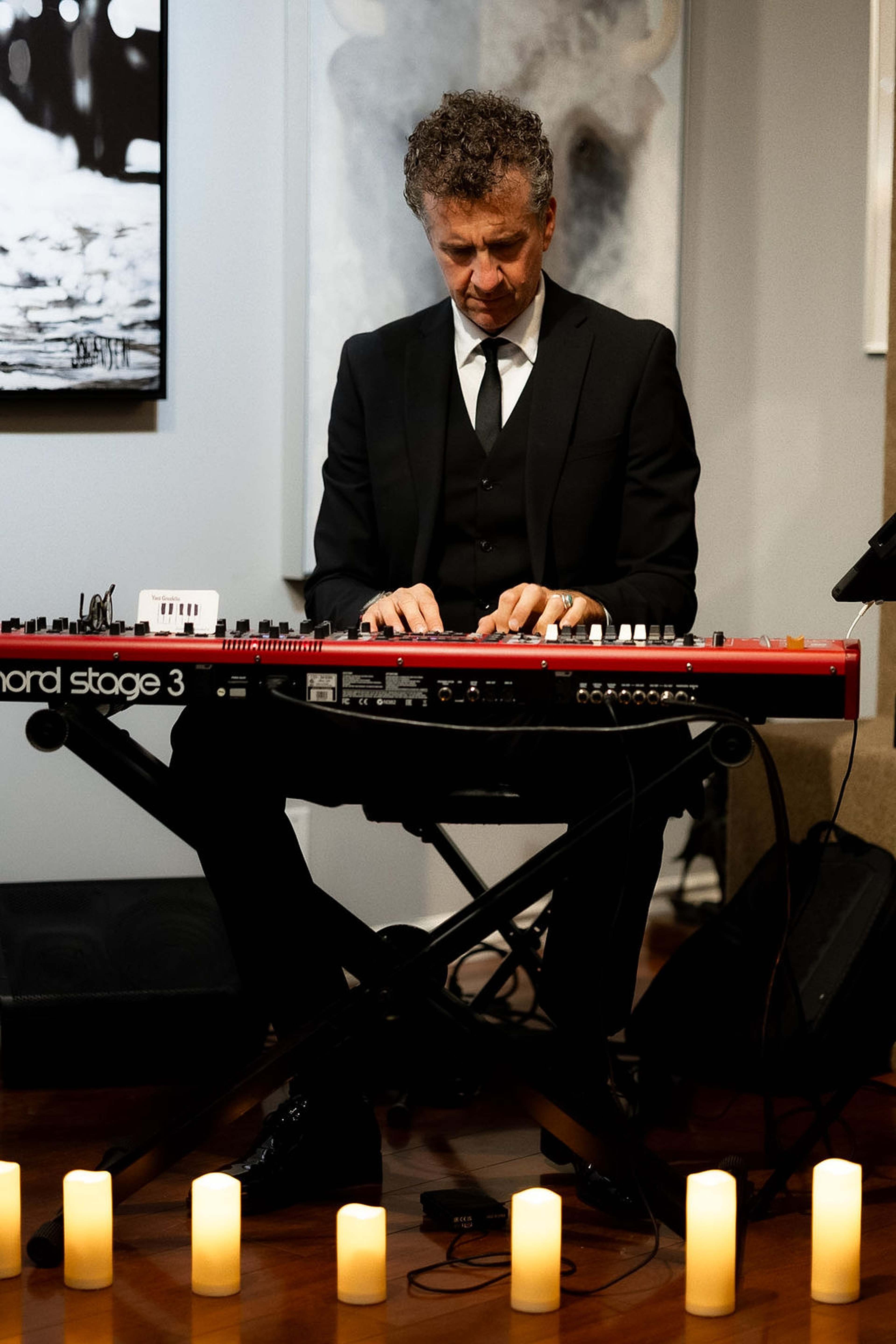 Musician playing a stage keyboard, candles set along the floor