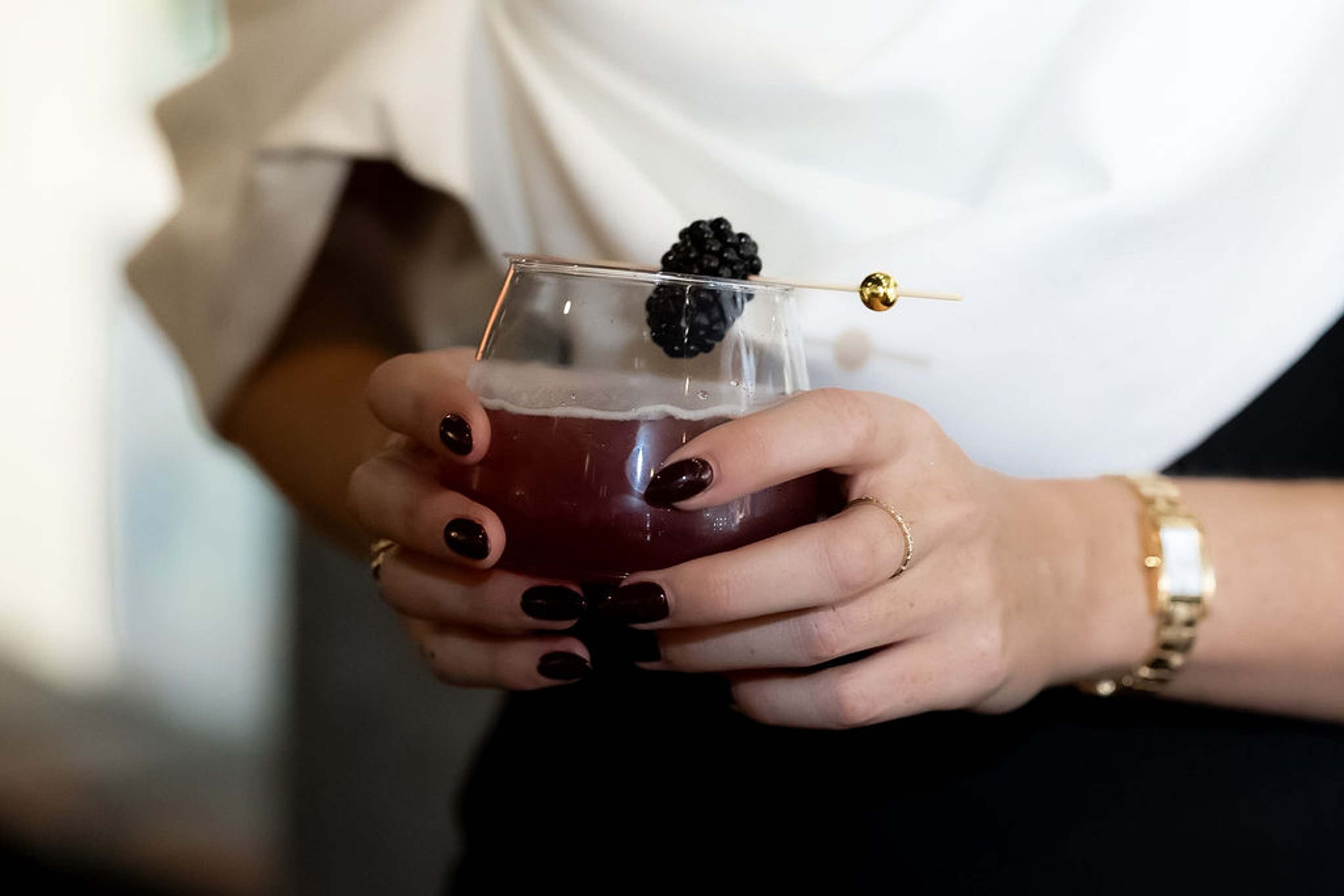 Close crop of hands holding a berry cocktail garnished with a blackberry
