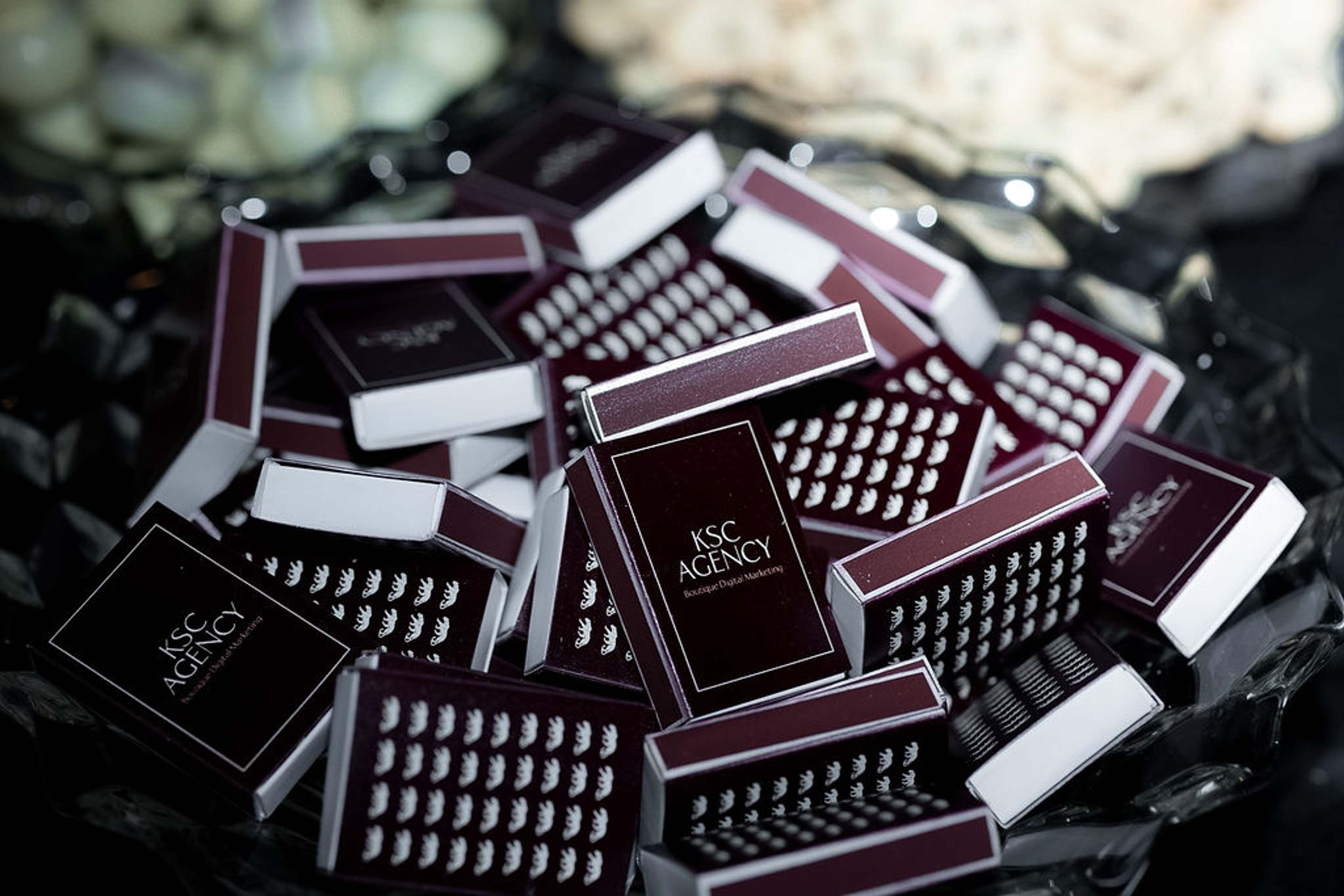 A scattered pile of KSC Agency branded chocolate bars in deep burgundy and black packaging