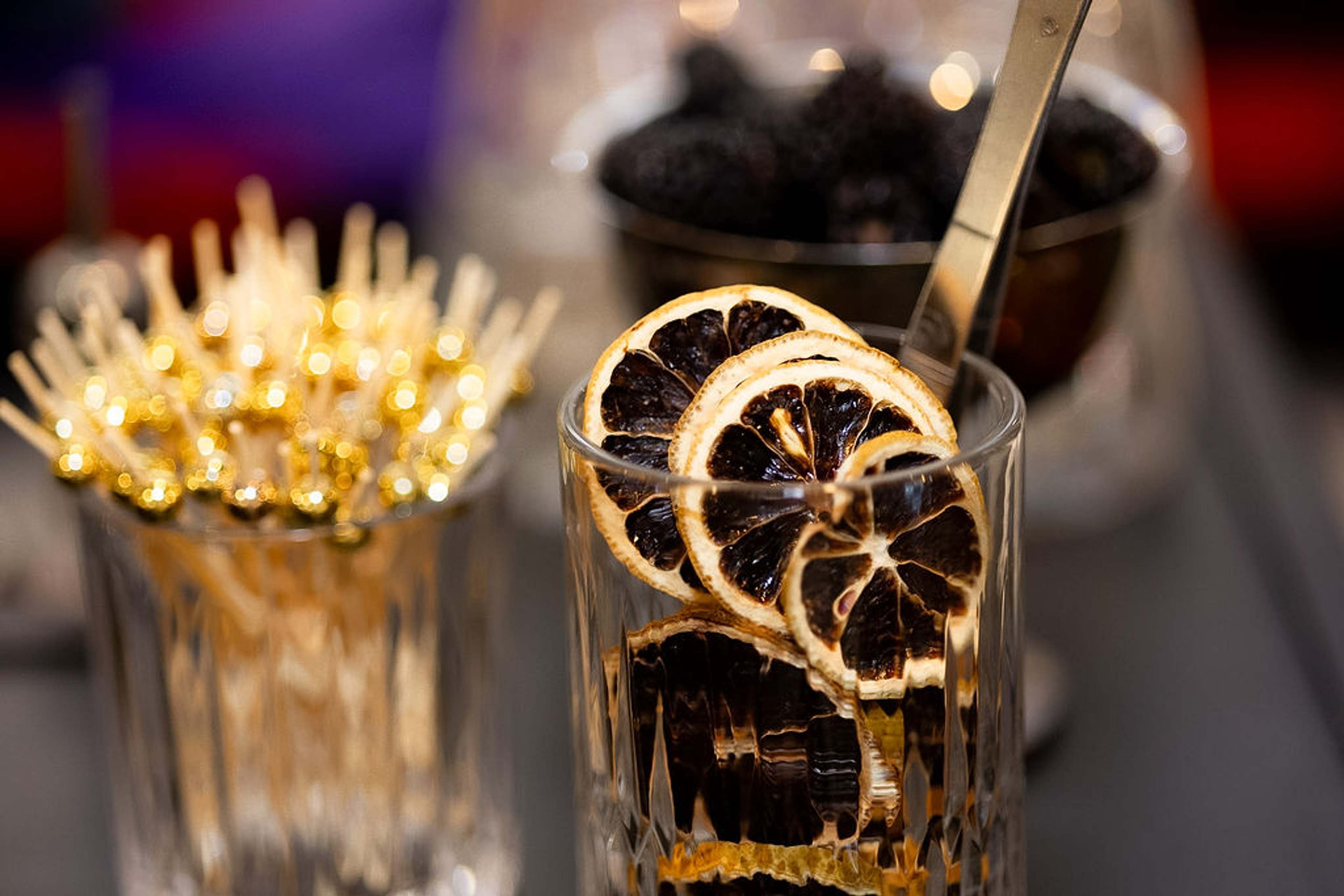 Cocktail garnished with dried orange wheels beside a jar of gold cocktail picks