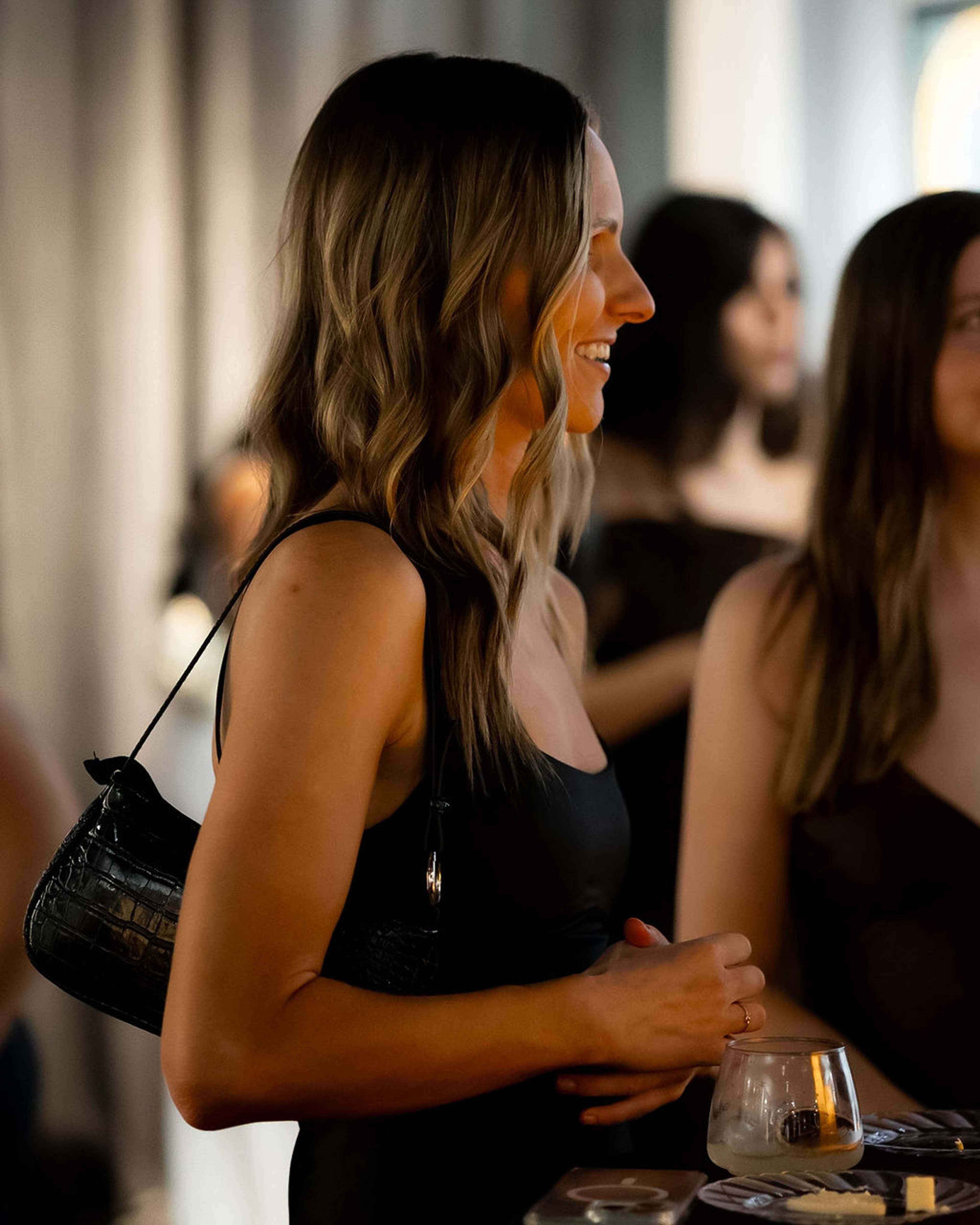 Guest laughing in profile, shoulder bag at her side