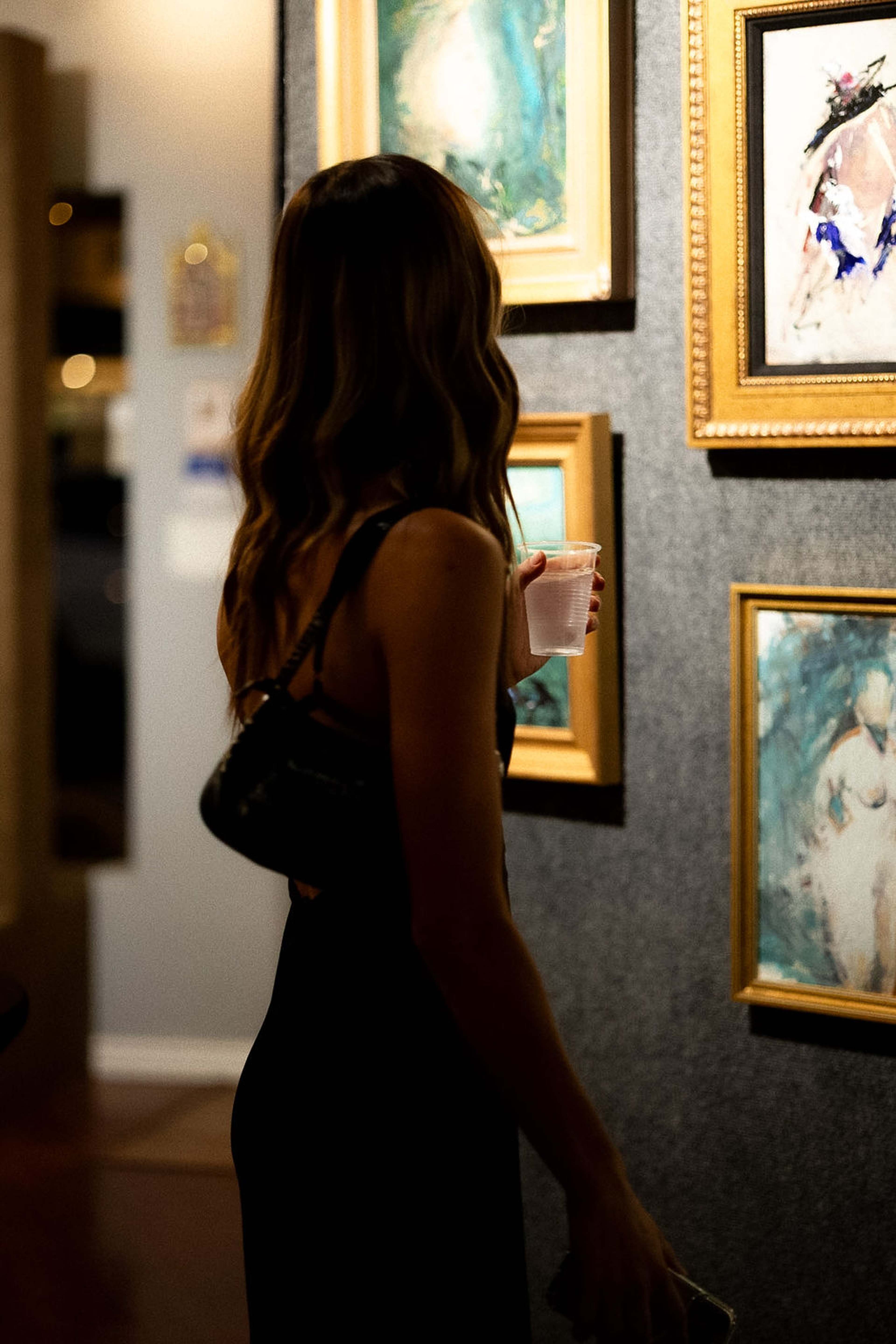 Guest looking at gold-framed paintings, drink in hand