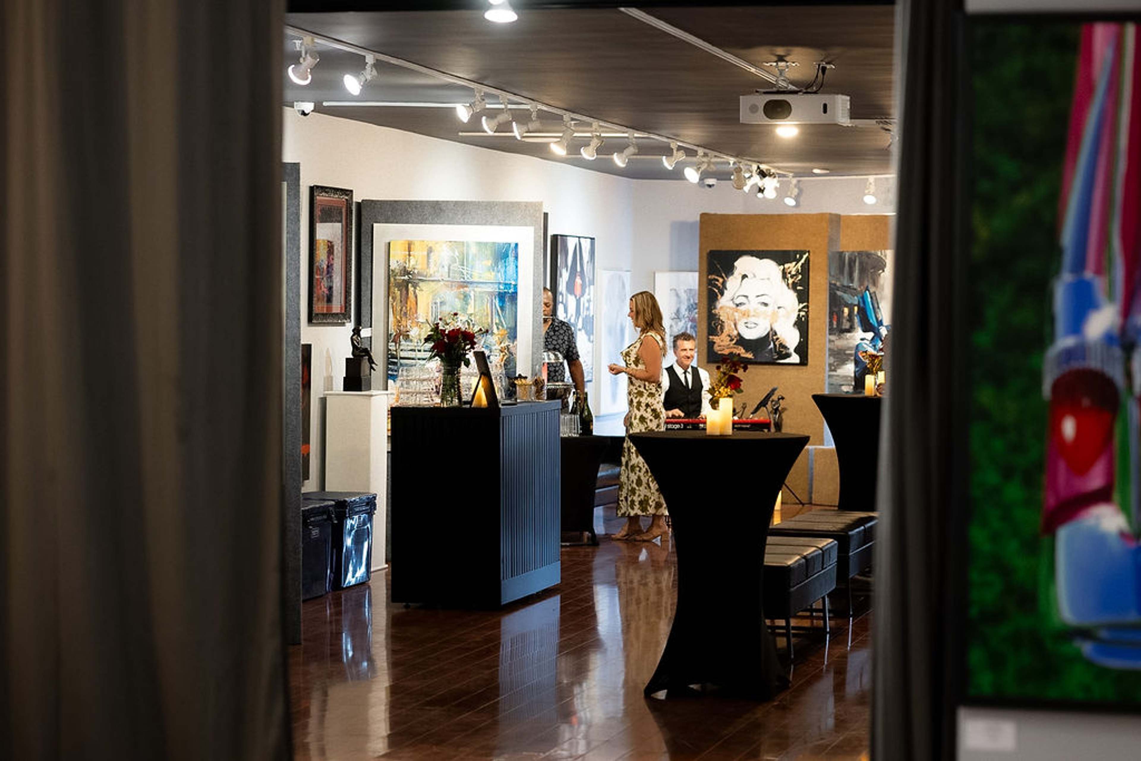 View through a curtain into the gallery, guests at cocktail tables under track lighting