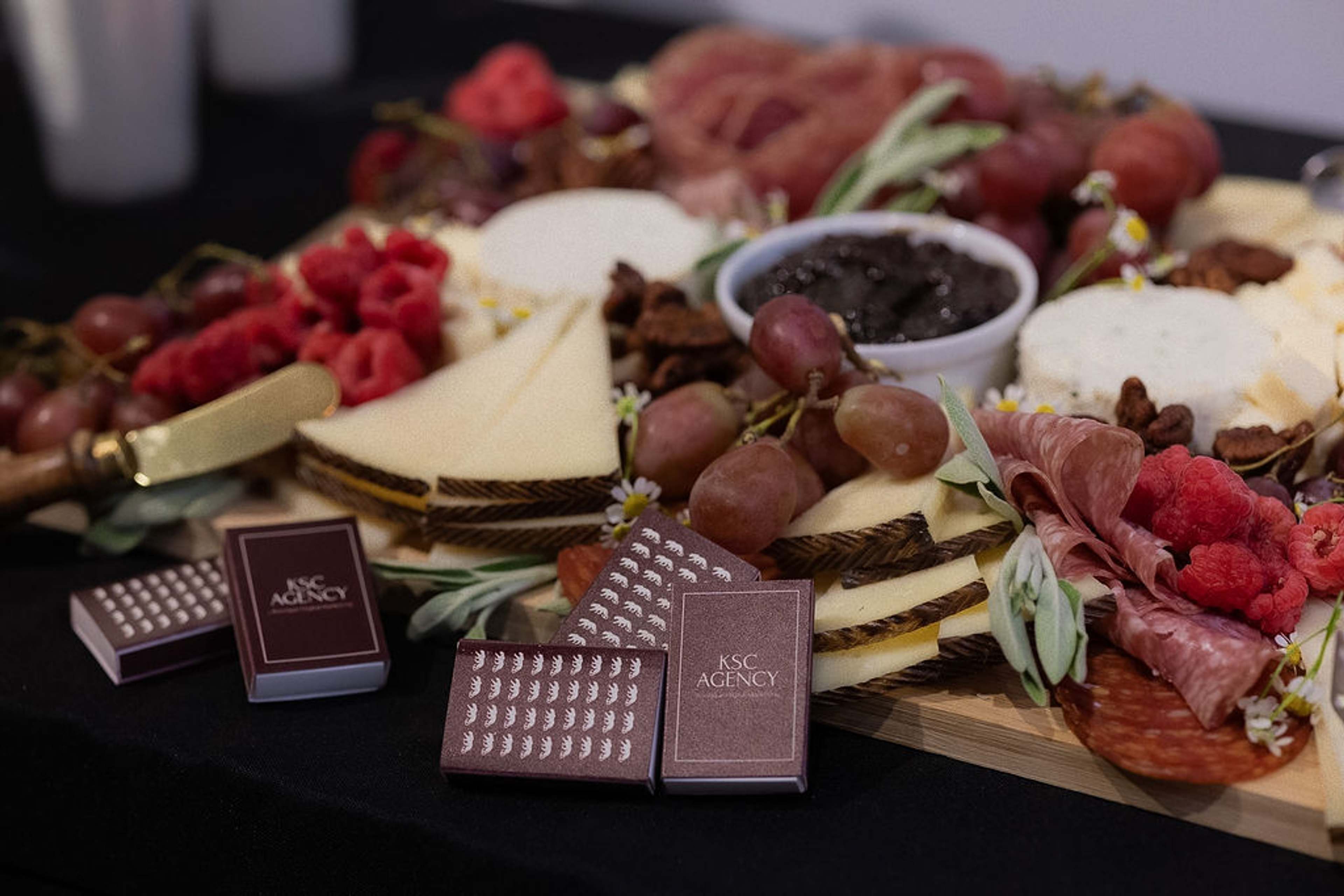 An overhead grazing board of cheeses, cured meats and grapes with KSC Agency branded chocolate