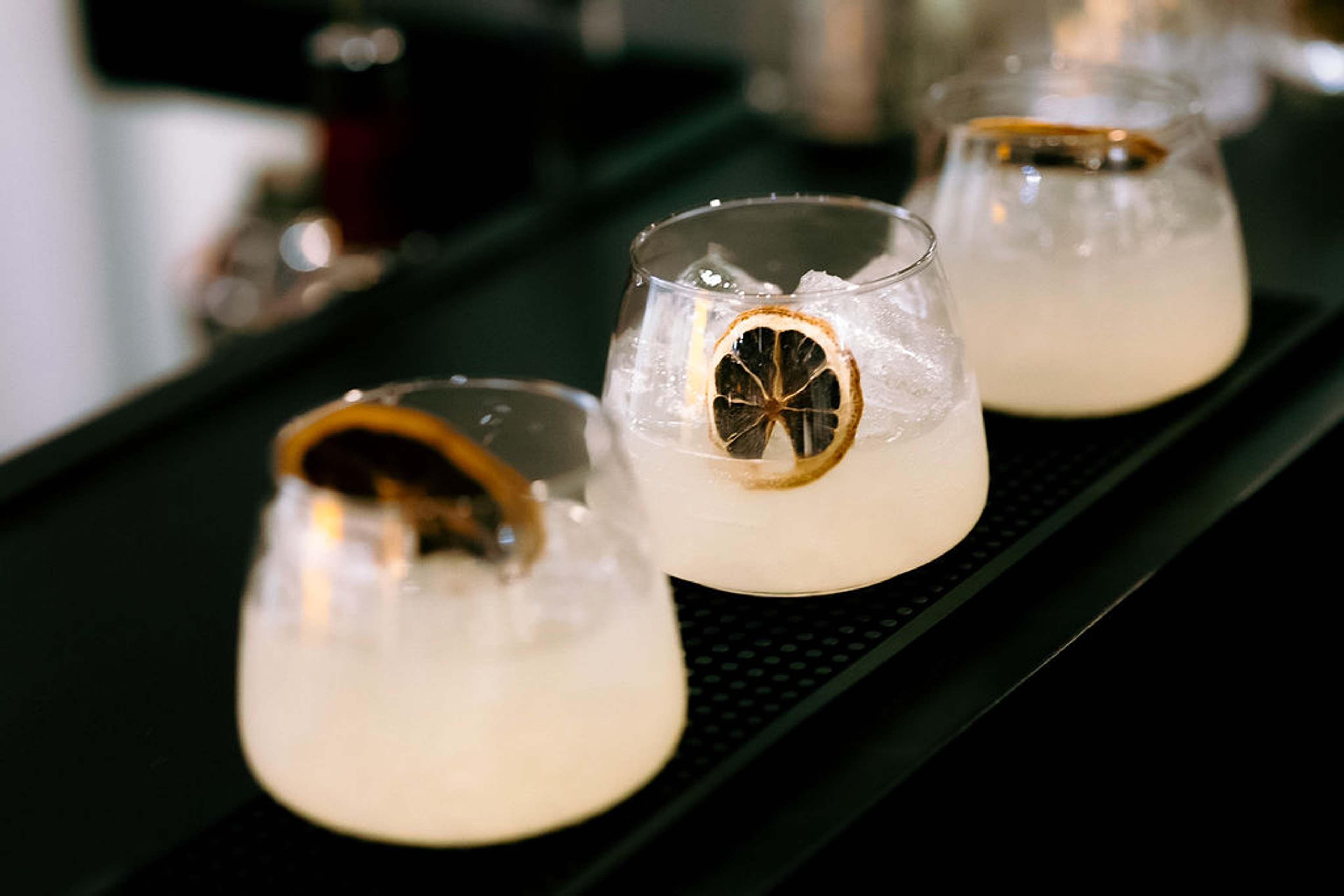 Two cocktails garnished with dehydrated citrus wheels, lit against a dark green backdrop