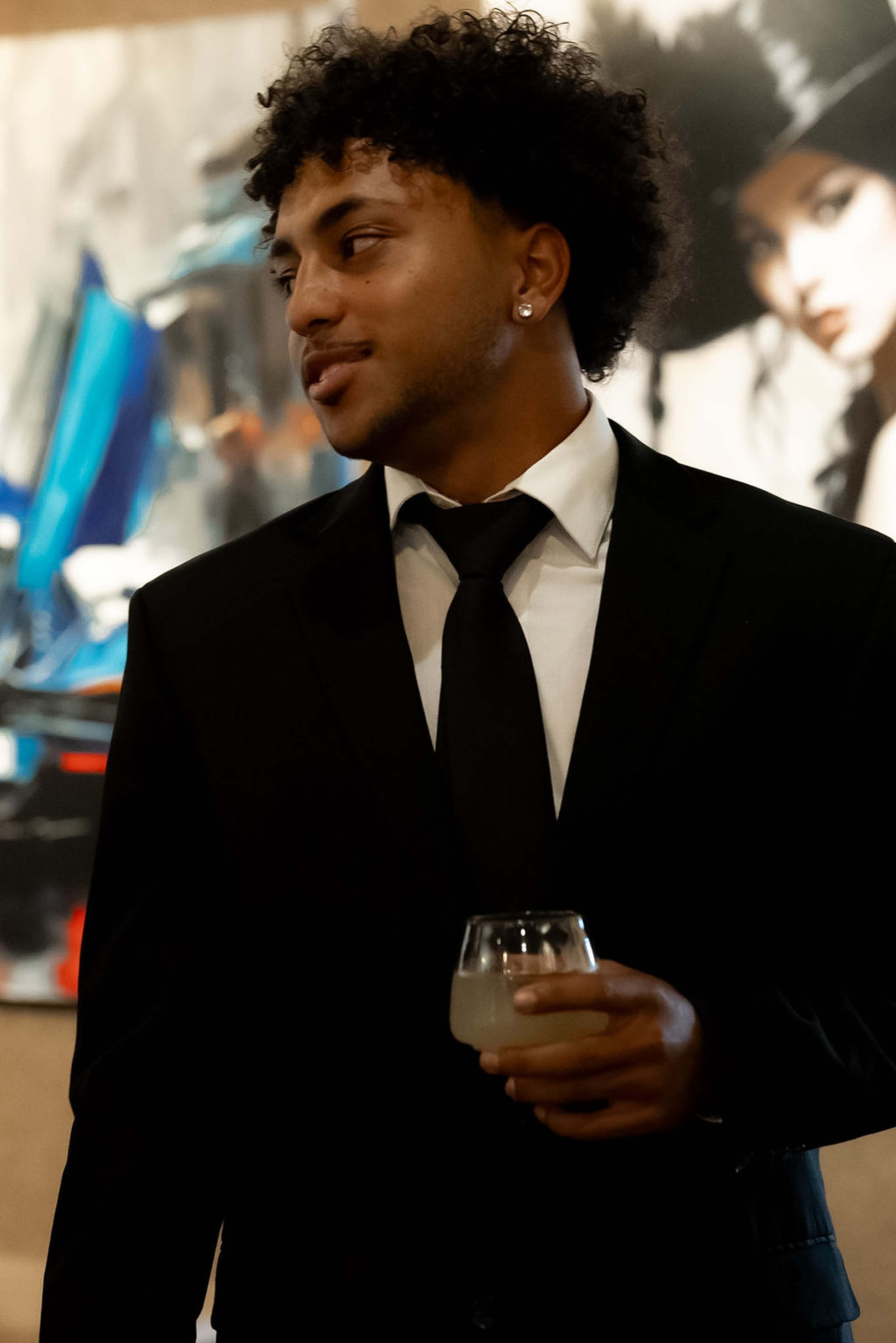 Guest in a black suit and tie holding a drink, artwork behind