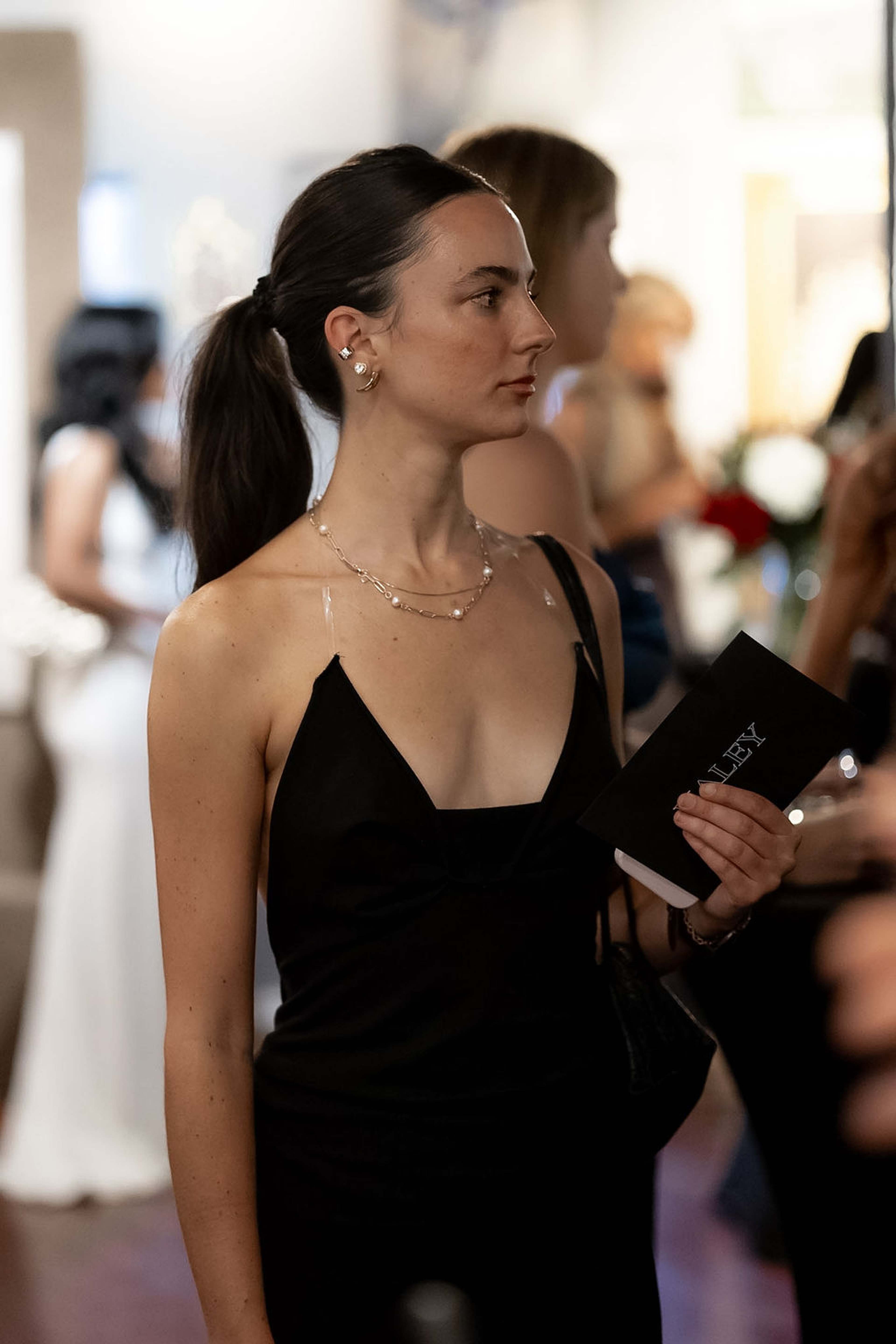 Guest in a black slip dress holding the event programme