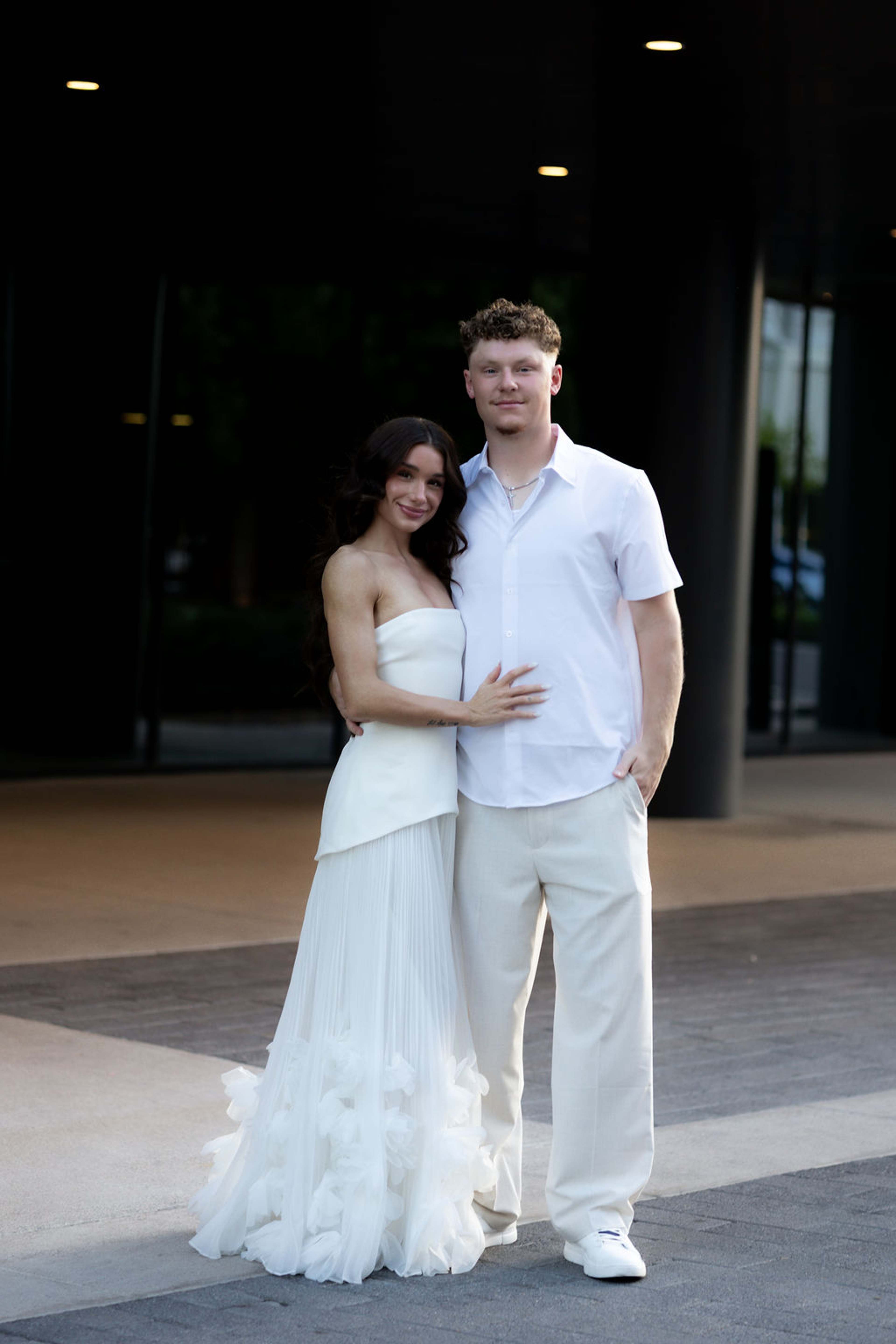 Full length frame of a couple standing together outside a pale stucco building at dusk